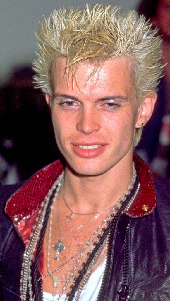 Person with spiky hair in a leather jacket layered over a sequined shirt, multiple necklaces visible