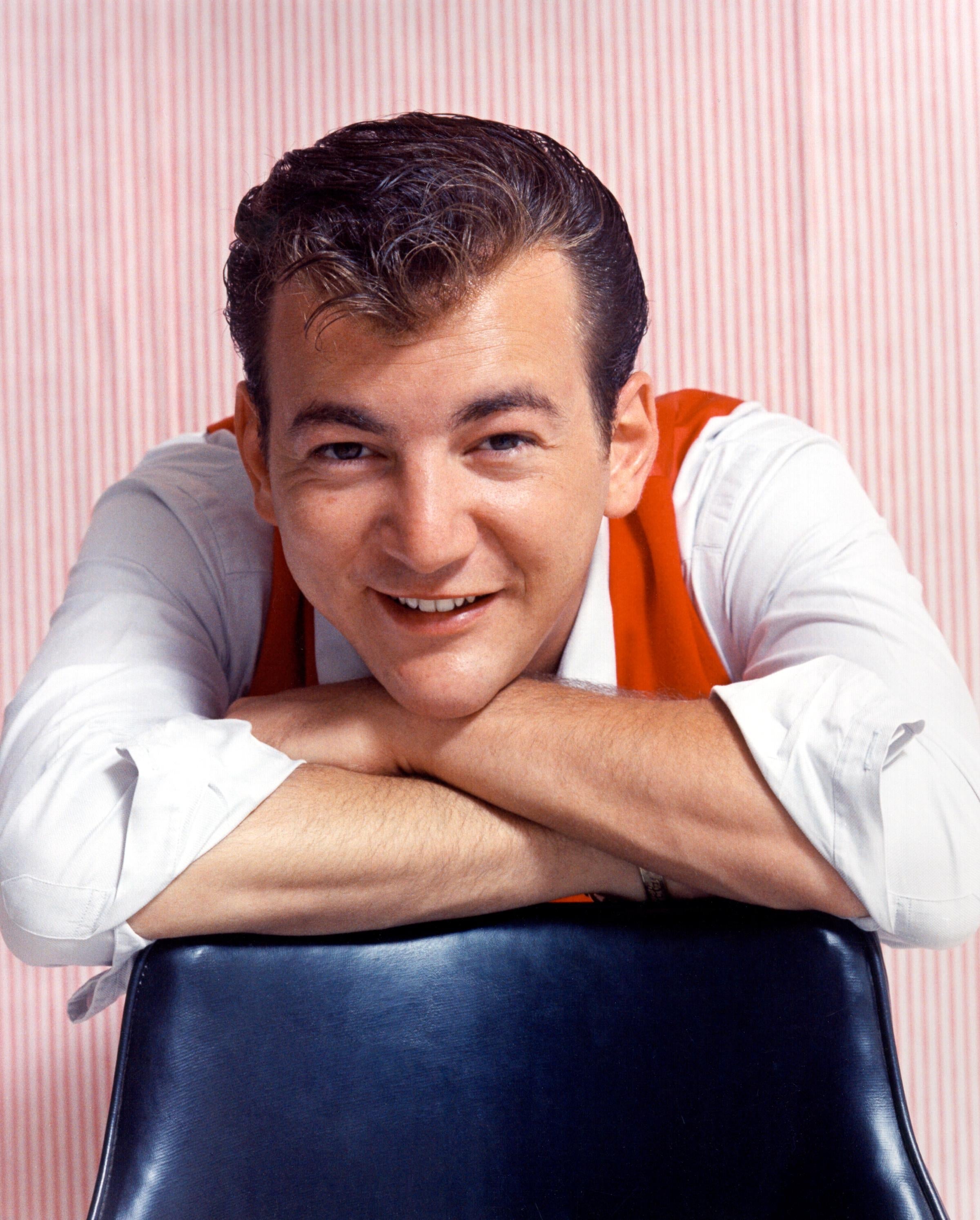 Person leaning on a chair, smiling, wearing a white shirt with a vest