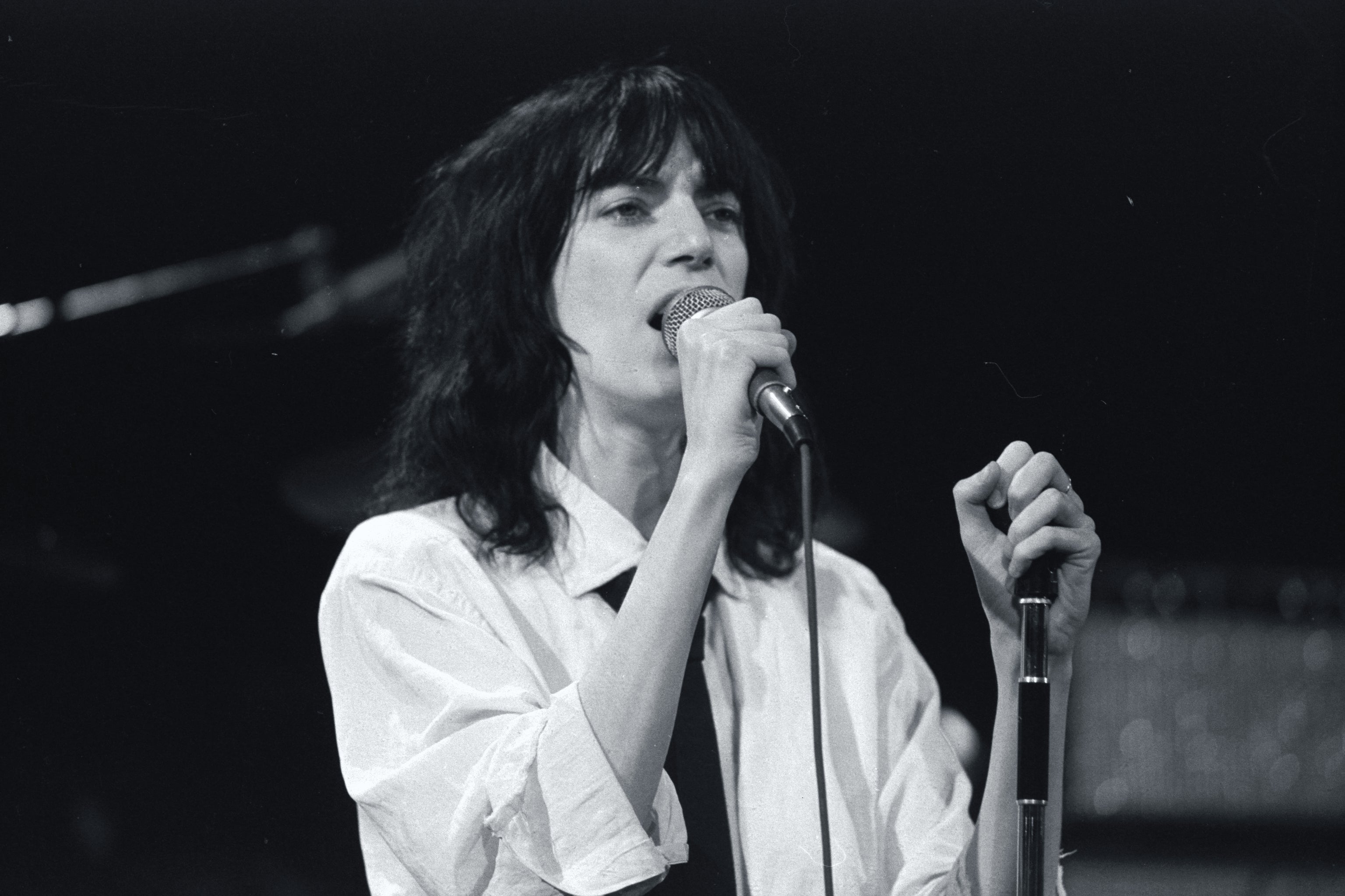 A person singings into a microphone, wearing a white shirt and tie, with a focused expression