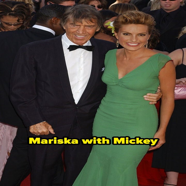 A man in a tuxedo and a woman in a fitted green dress pose together on a red carpet