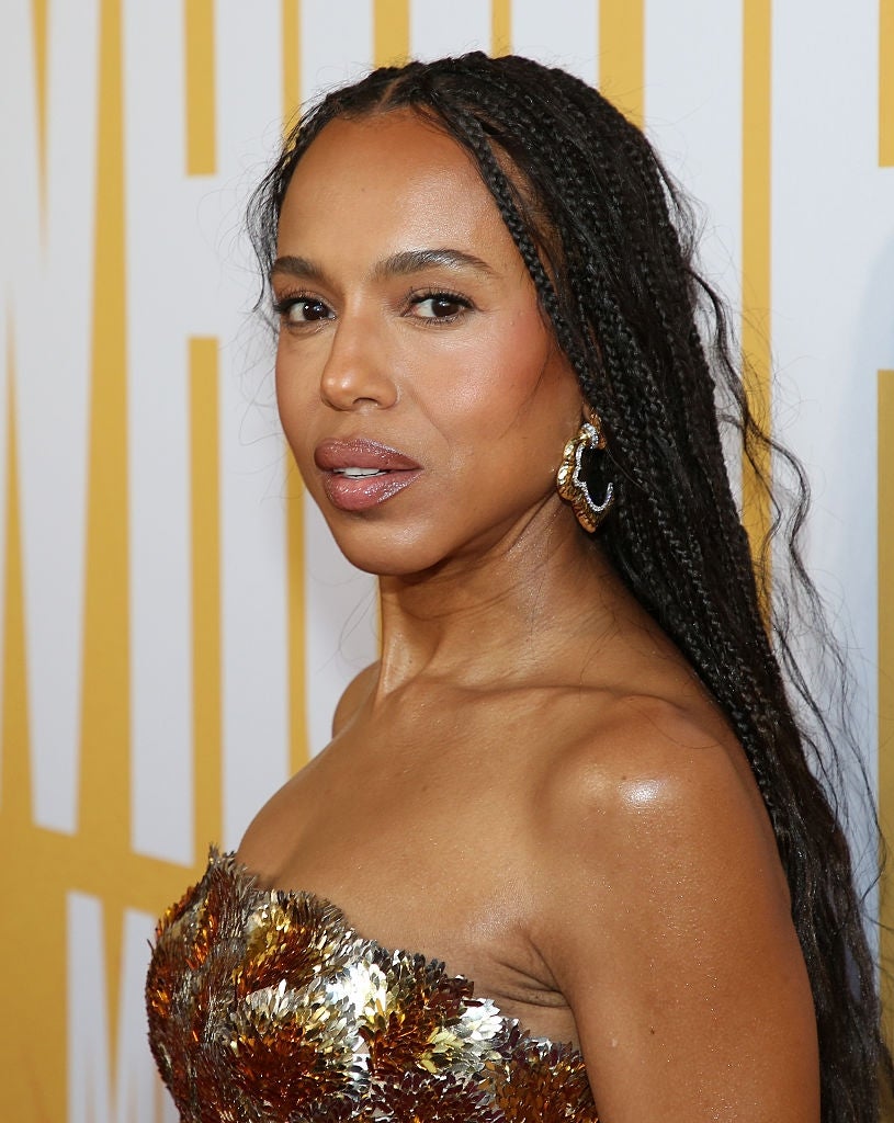 Person in a strapless gown with braided hair attends an event, standing in front of a large text background