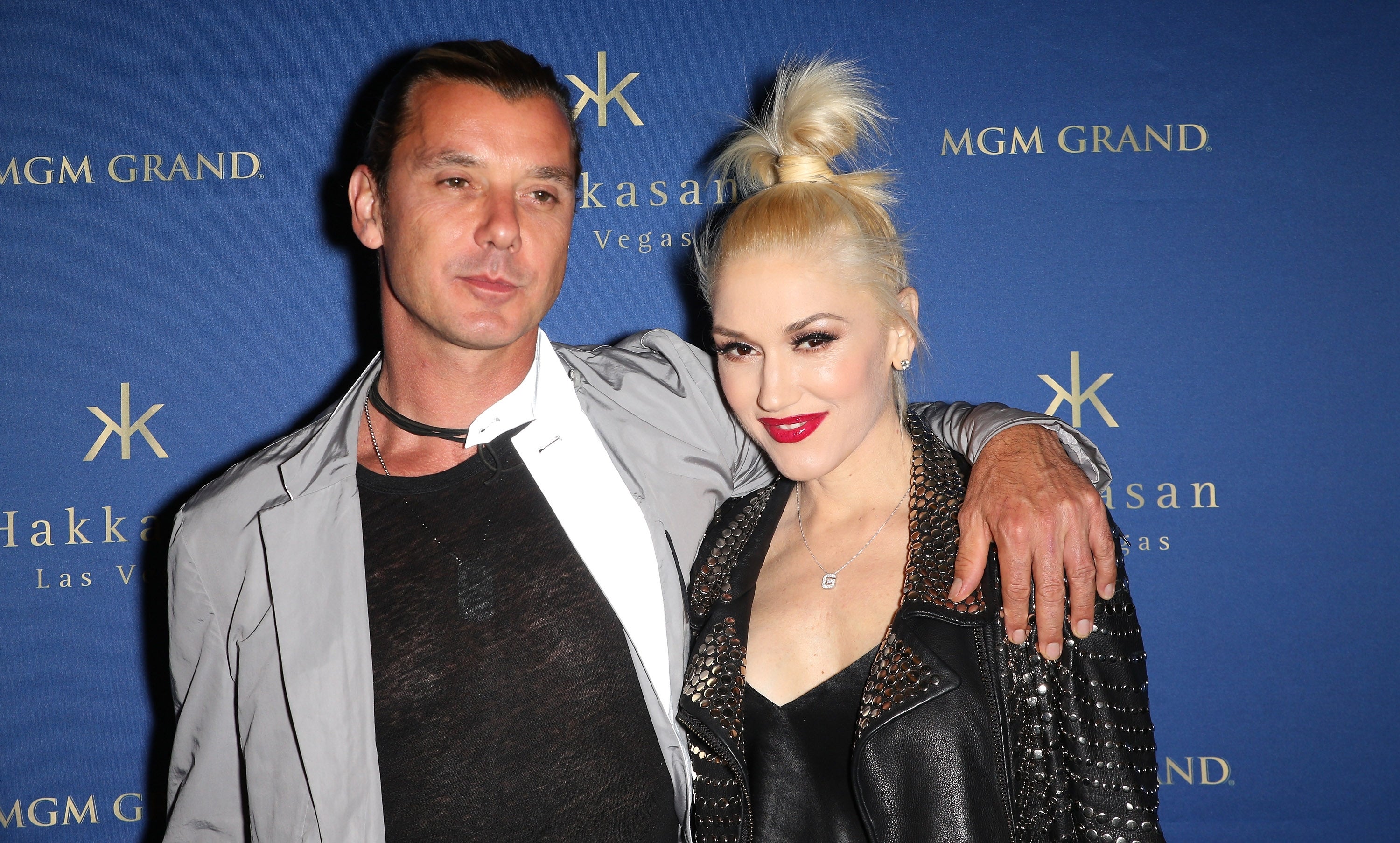 Two people pose on the red carpet. One wears a leather jacket with spiked studs, and the other wears a casual shirt and jacket