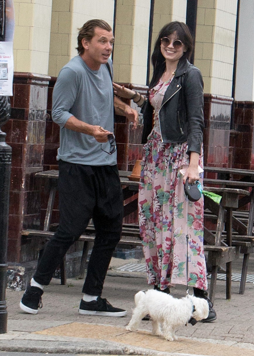Two people casually dressed with a small white dog on a leash. The person on the right wears a floral dress and a black leather jacket