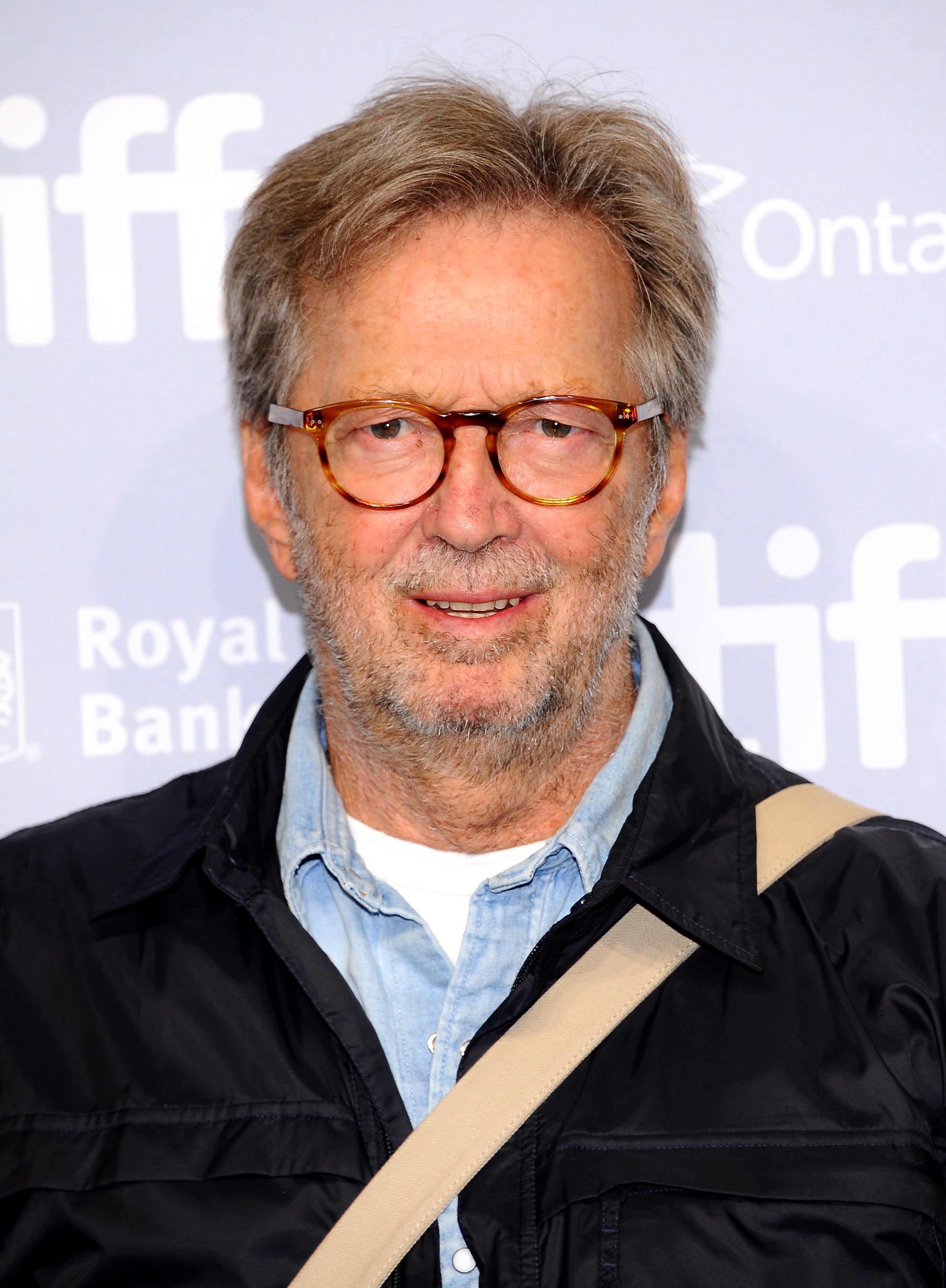 Man with glasses wearing a casual jacket over a denim shirt, smiling at a film festival backdrop