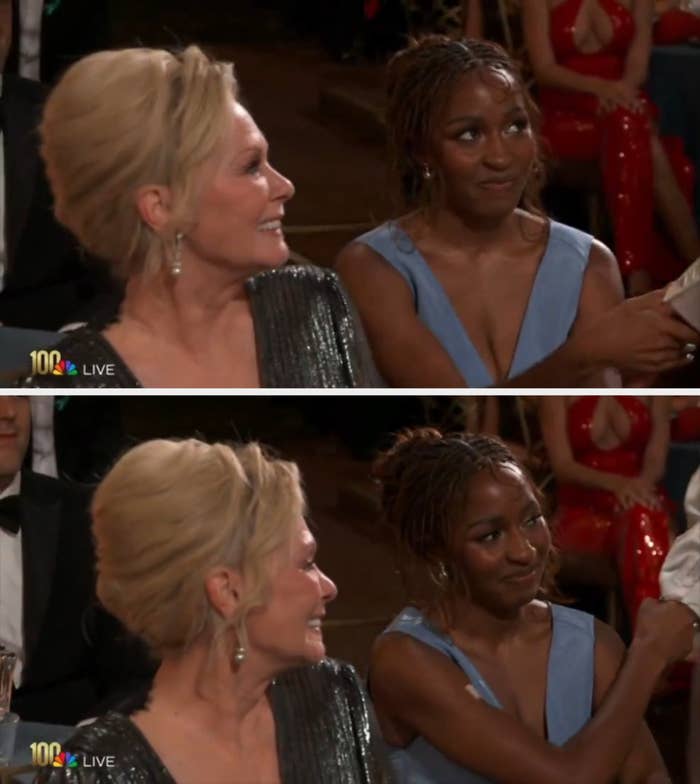 Two women at an awards event; one in a sparkly dress, the other in a sleeveless gown, both smiling and looking towards the stage