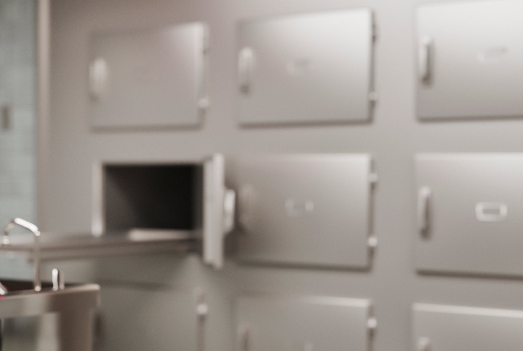 A mannequin on a metal table in a clinical, tiled room with lockers and a weighing scale, resembling a medical or laboratory setting