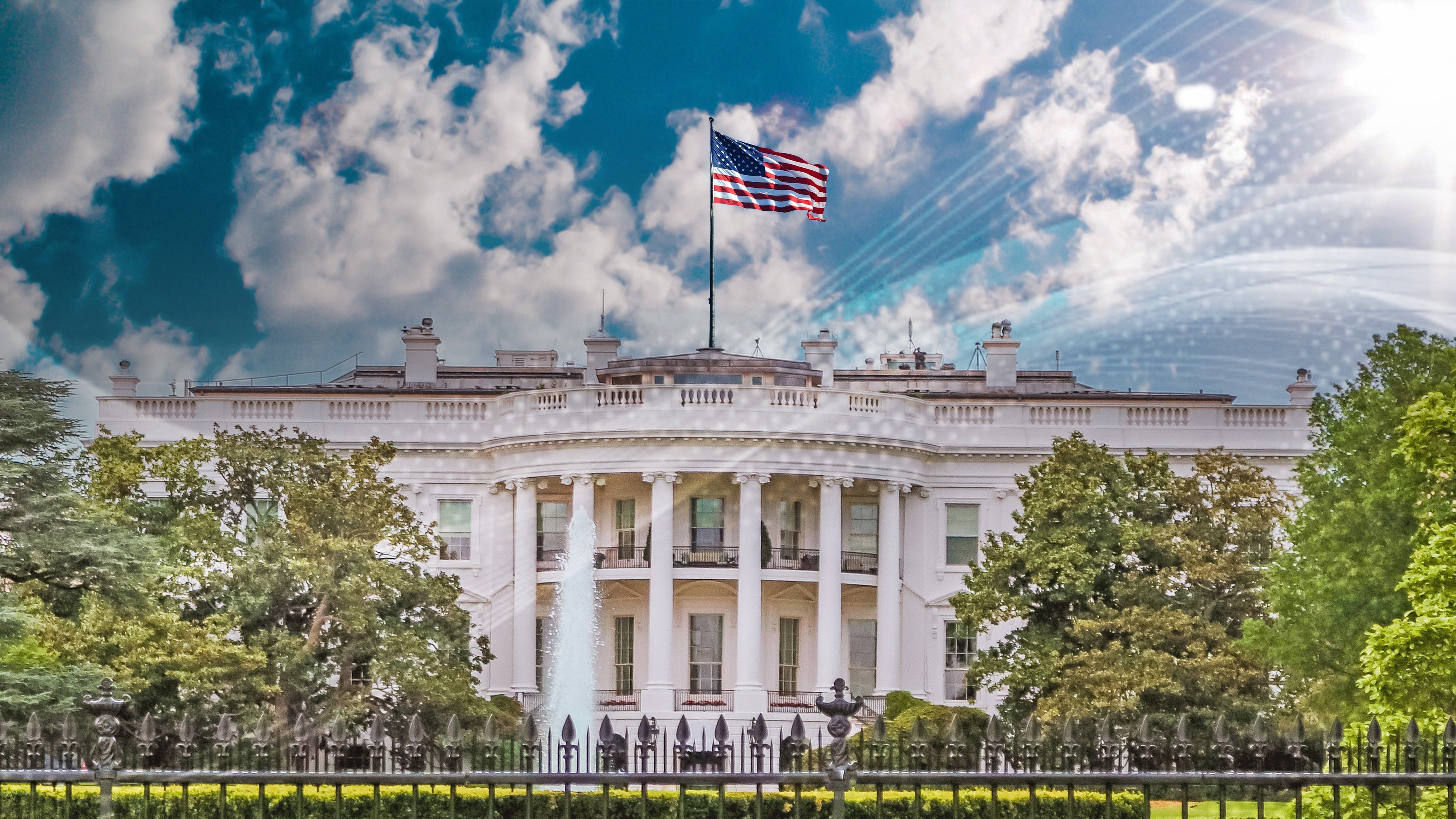 The White House with an American flag on top, surrounded by trees and a bright sun in the sky