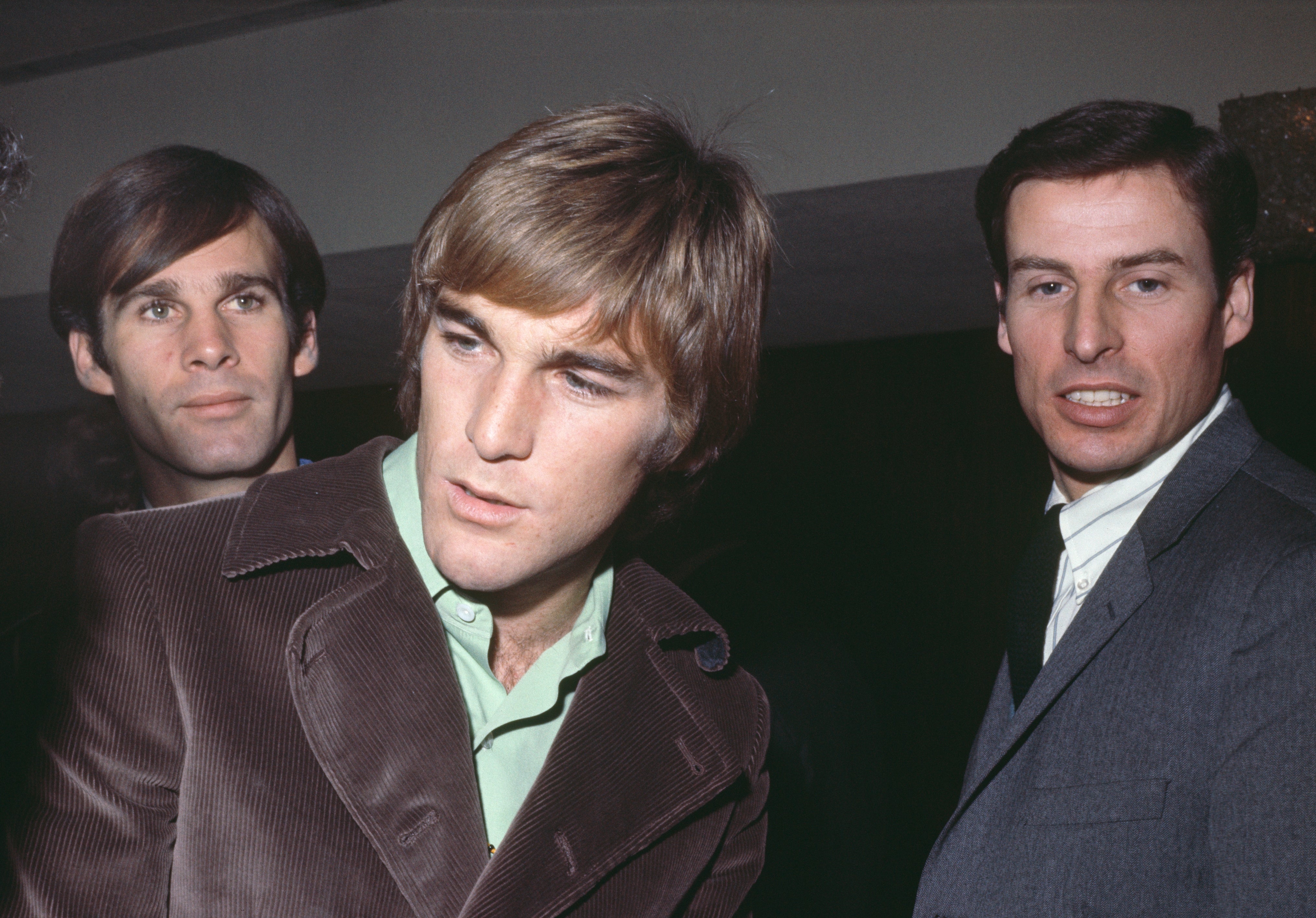 Three men in vintage suits are captured in conversation at an event, looking towards someone off-camera