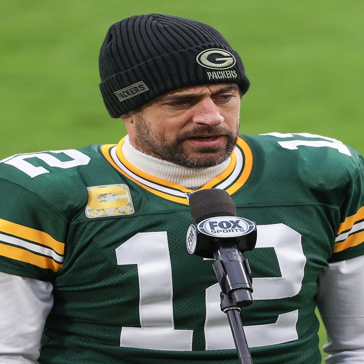 Person in a sports jersey and beanie speaks into a microphone on a football field