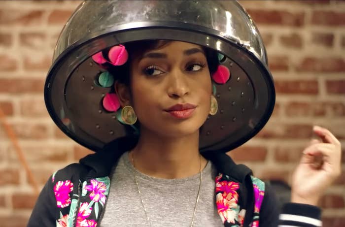 Person under hair dryer with colorful curlers, wearing floral jacket
