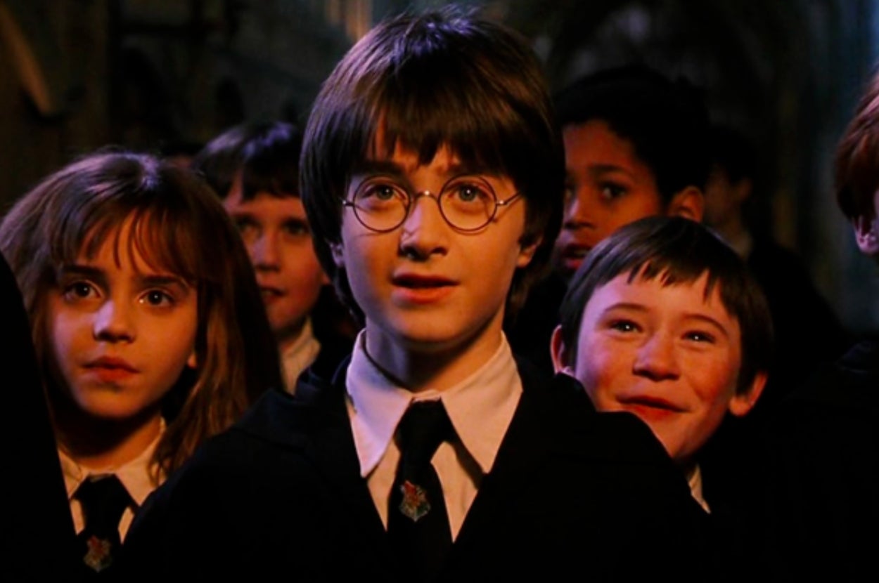 A group of young Hogwarts students in wizard attire look excitedly ahead, Harry and Hermione at the front of the group