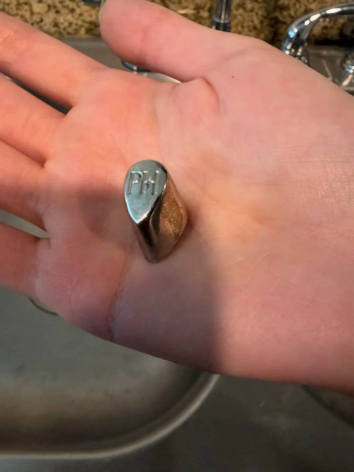 Person holding a metal pH sliding-weight for a knife on their palm, with a kitchen sink in the background