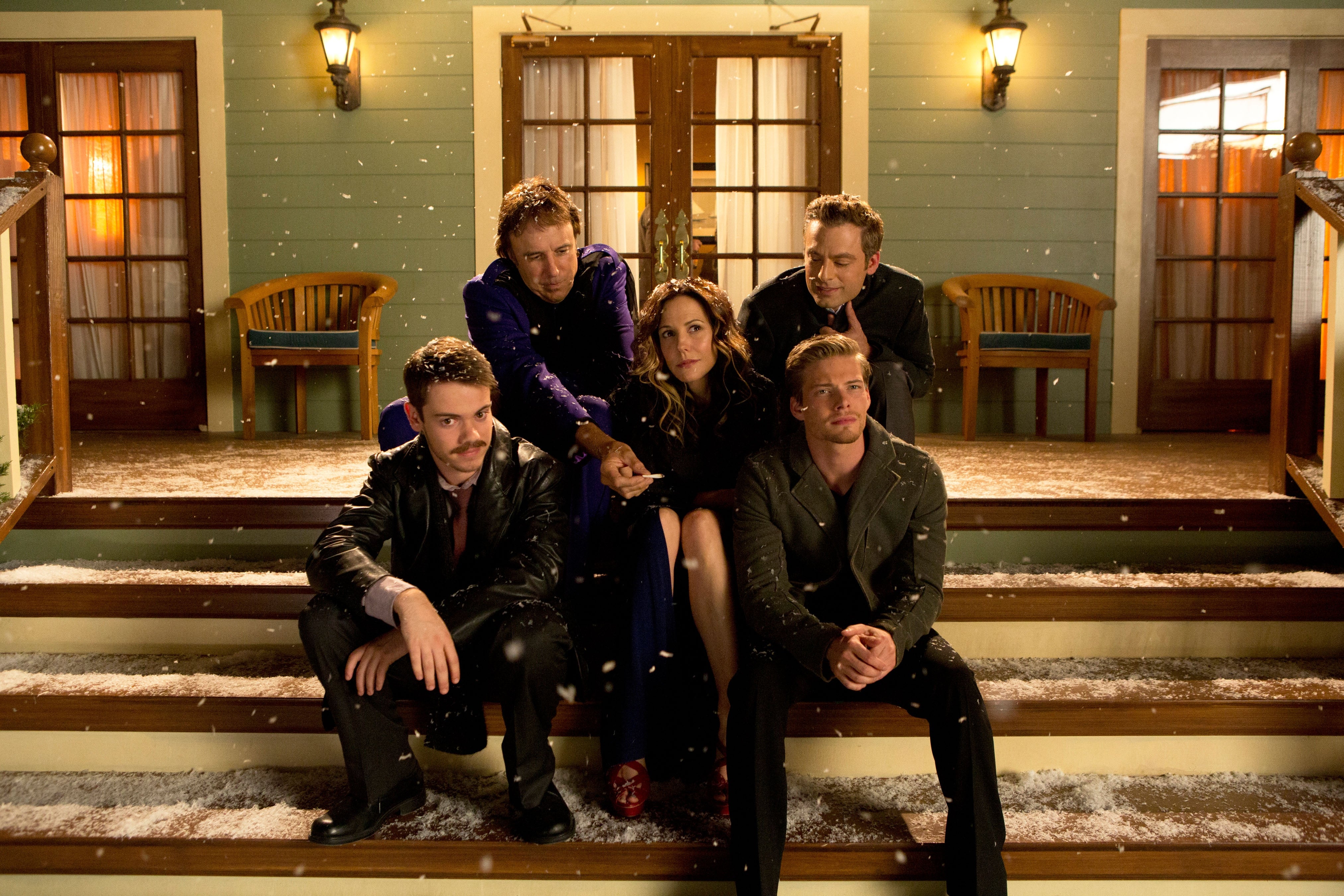 Cast of a TV show sitting on house steps in winter attire, posing for a promotional photo