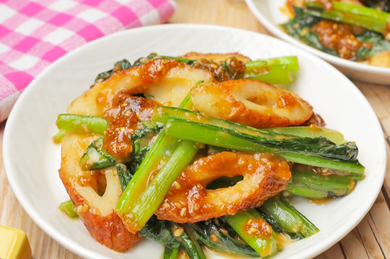 皿に盛られたちくわと青菜の炒め物。テーブルにピンクのチェック柄の布と箸が添えられている。