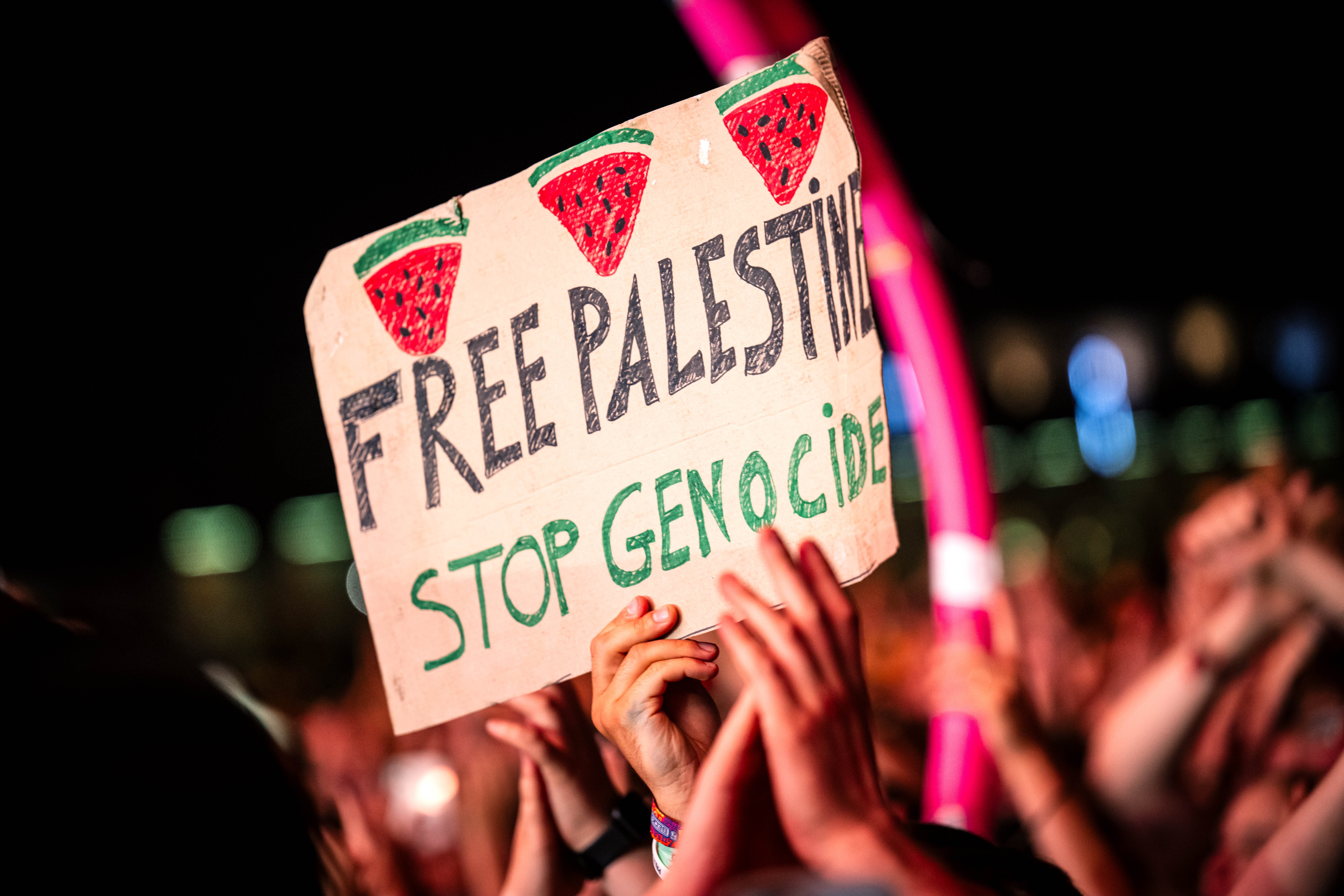 Skilt med «Fri Palestina, Stopp folkemord»," holdt av en folkemengde. Dekorert med vannmelontegninger