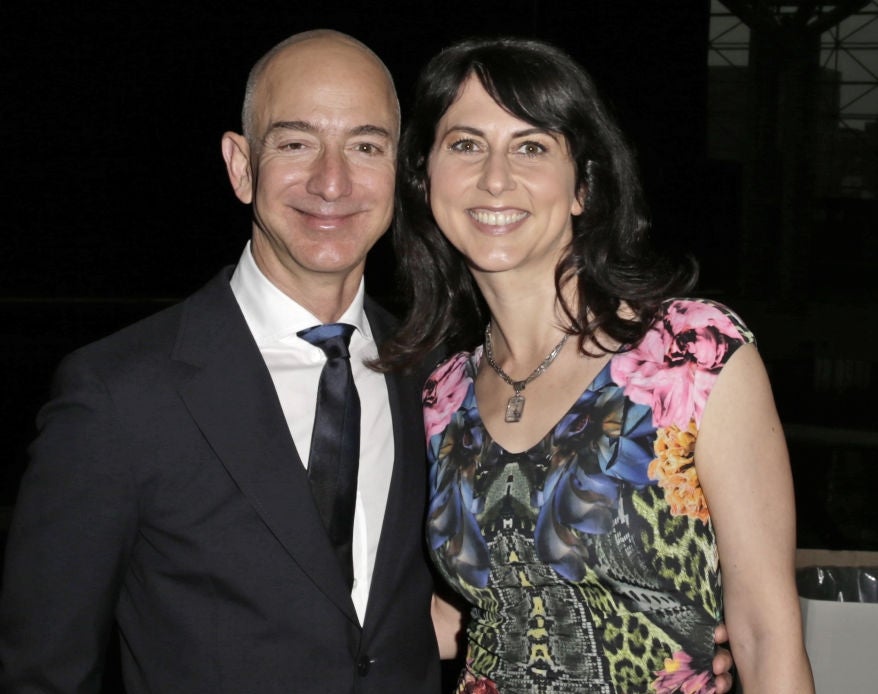 A man in a formal suit and a woman in a patterned dress with floral and animal print smile for the camera at an event