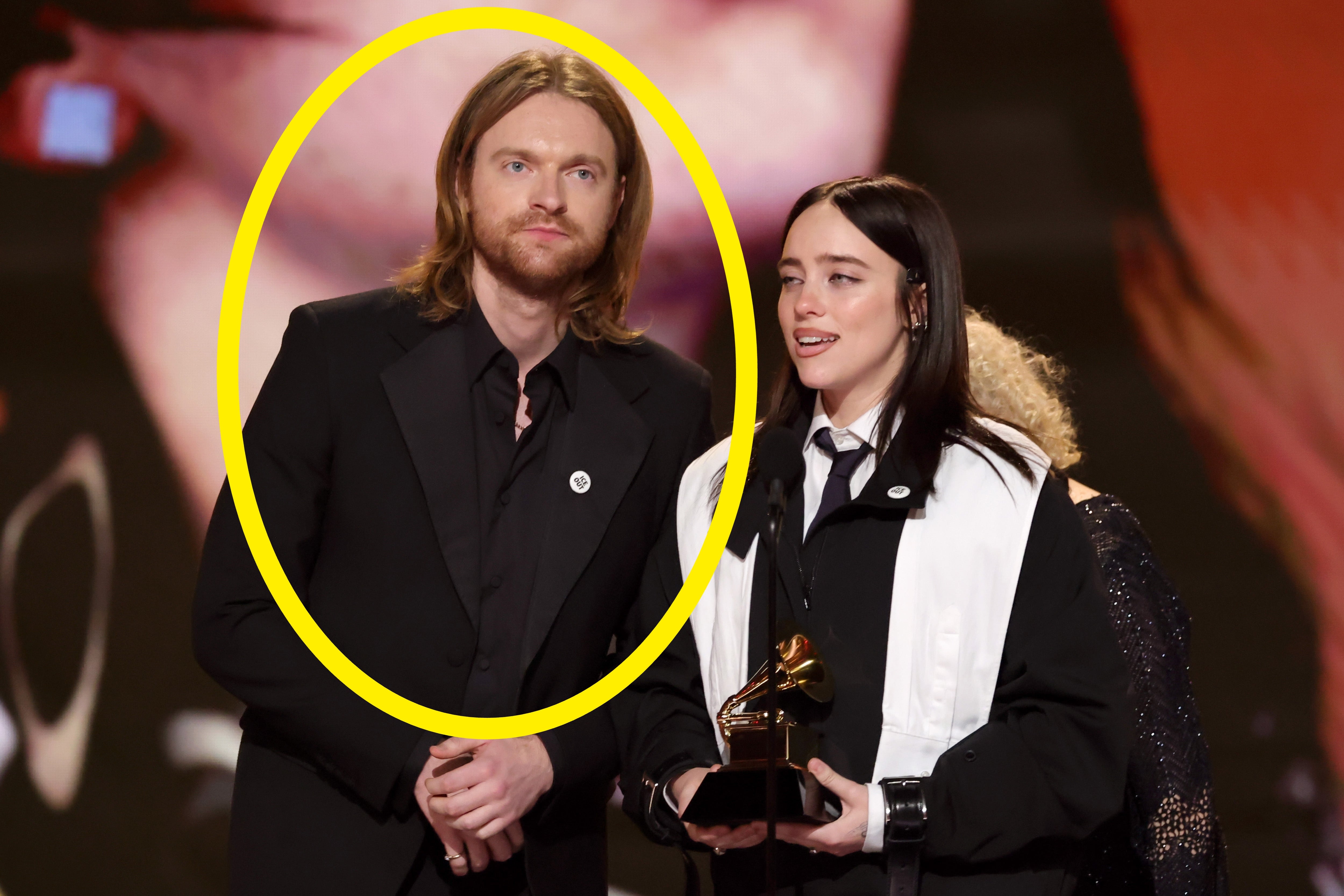 To personer står på scenen og holder en Grammy-pris, iført formelle svarte antrekk med hvite aksenter