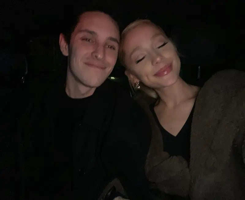 Two people smiling with closed eyes, sitting closely together. The person on the right is wrapped in a cozy garment