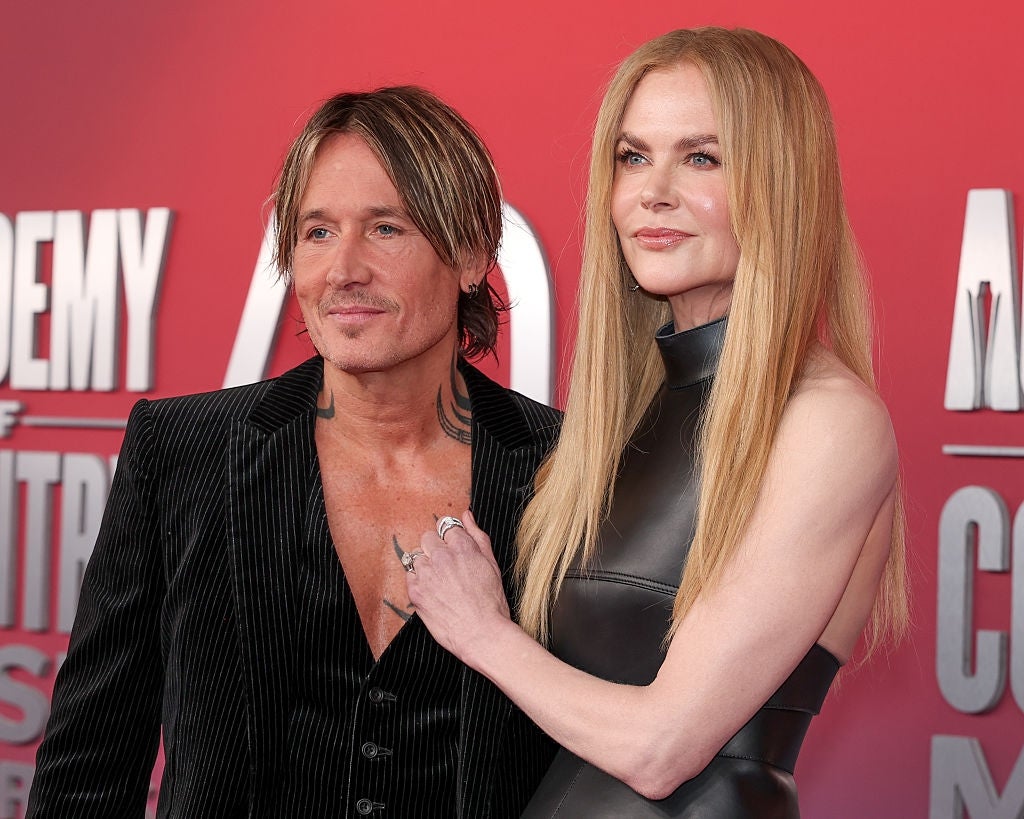 Two individuals on the red carpet. The man wears a pinstripe suit; the woman wears a sleeveless, high-neck dress. They pose arm-in-arm, smiling