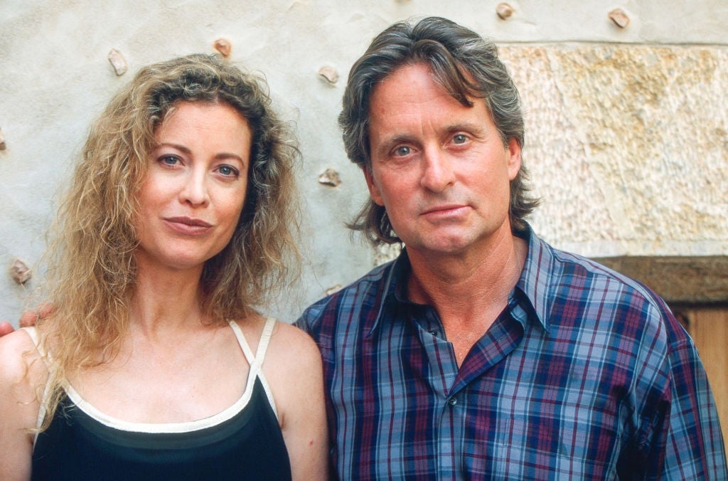 A man and woman standing close together, both with wavy hair. The man wears a plaid shirt; the woman is in a sleeveless top