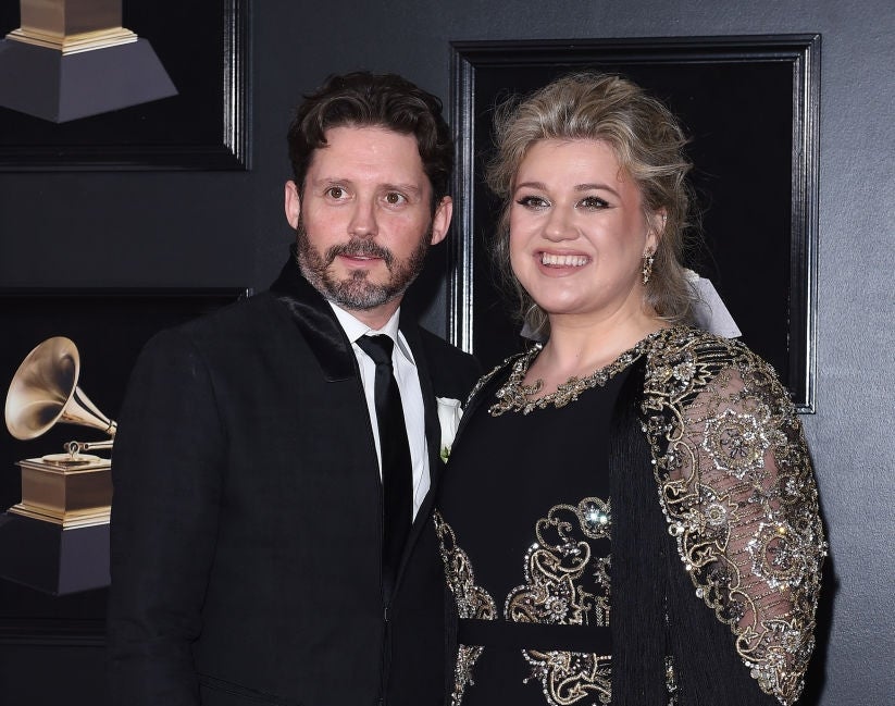 Two people pose at a red carpet event, with one wearing a black suit and the other in an ornate black dress adorned with decorative details