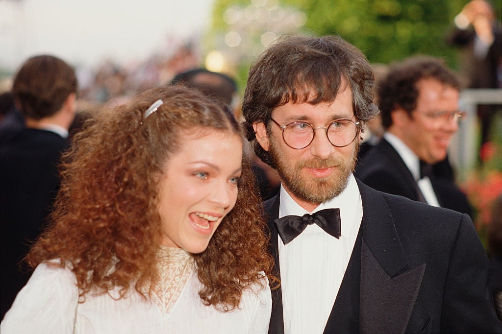 A woman with curly hair smiles next to a bearded man in glasses and a tuxedo at a formal event