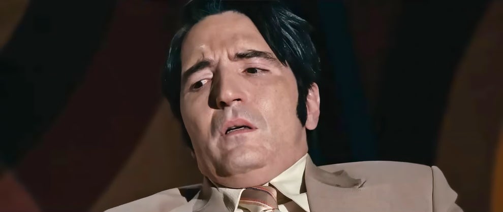 Person in a beige suit and tie with a concerned expression