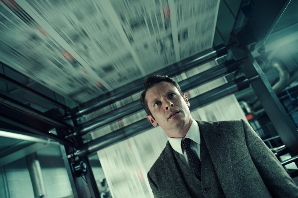 A person in a suit observes a fast-moving printing press in an industrial setting