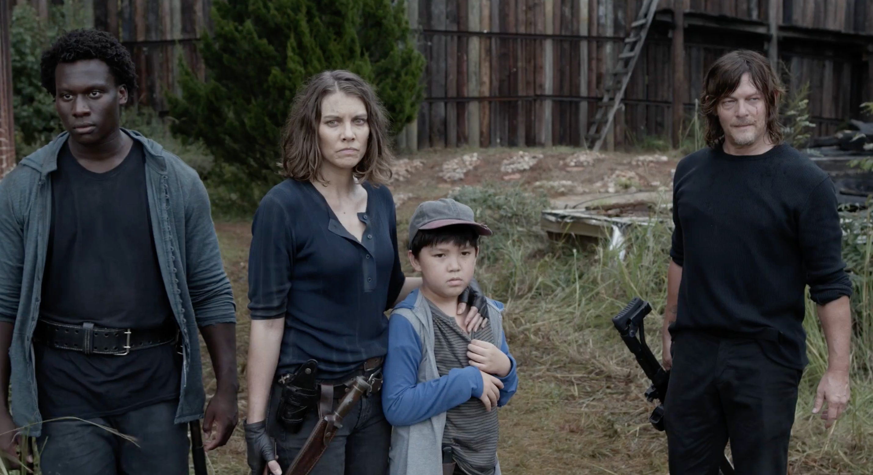 Four characters from a TV show stand outdoors, looking serious. They're dressed in rugged, survival-style clothing with weapons visible
