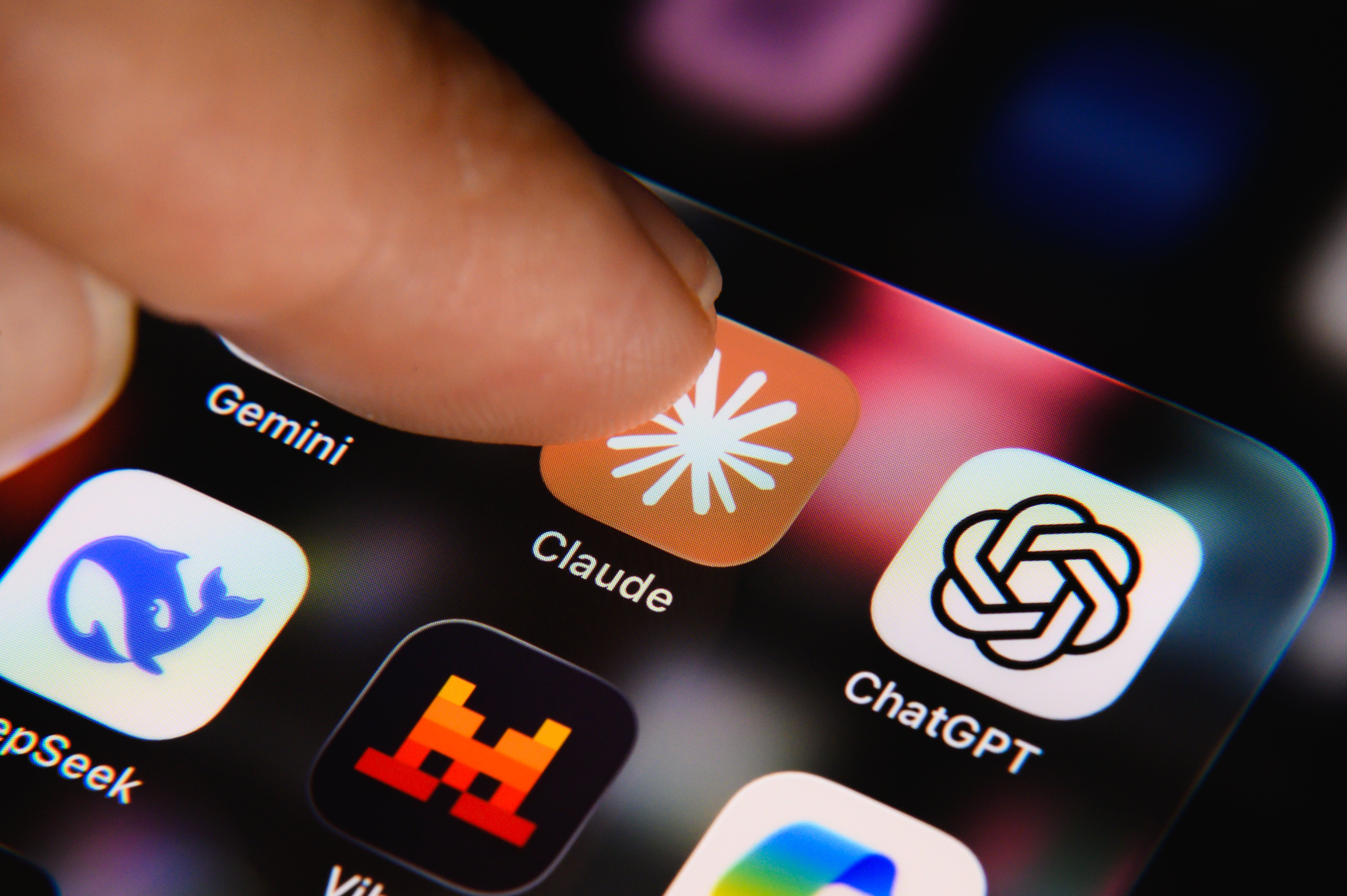 En finger berører Claude-appikonet på en smarttelefonskjerm, omgitt av andre appikoner som ChatGPT og Gemini
