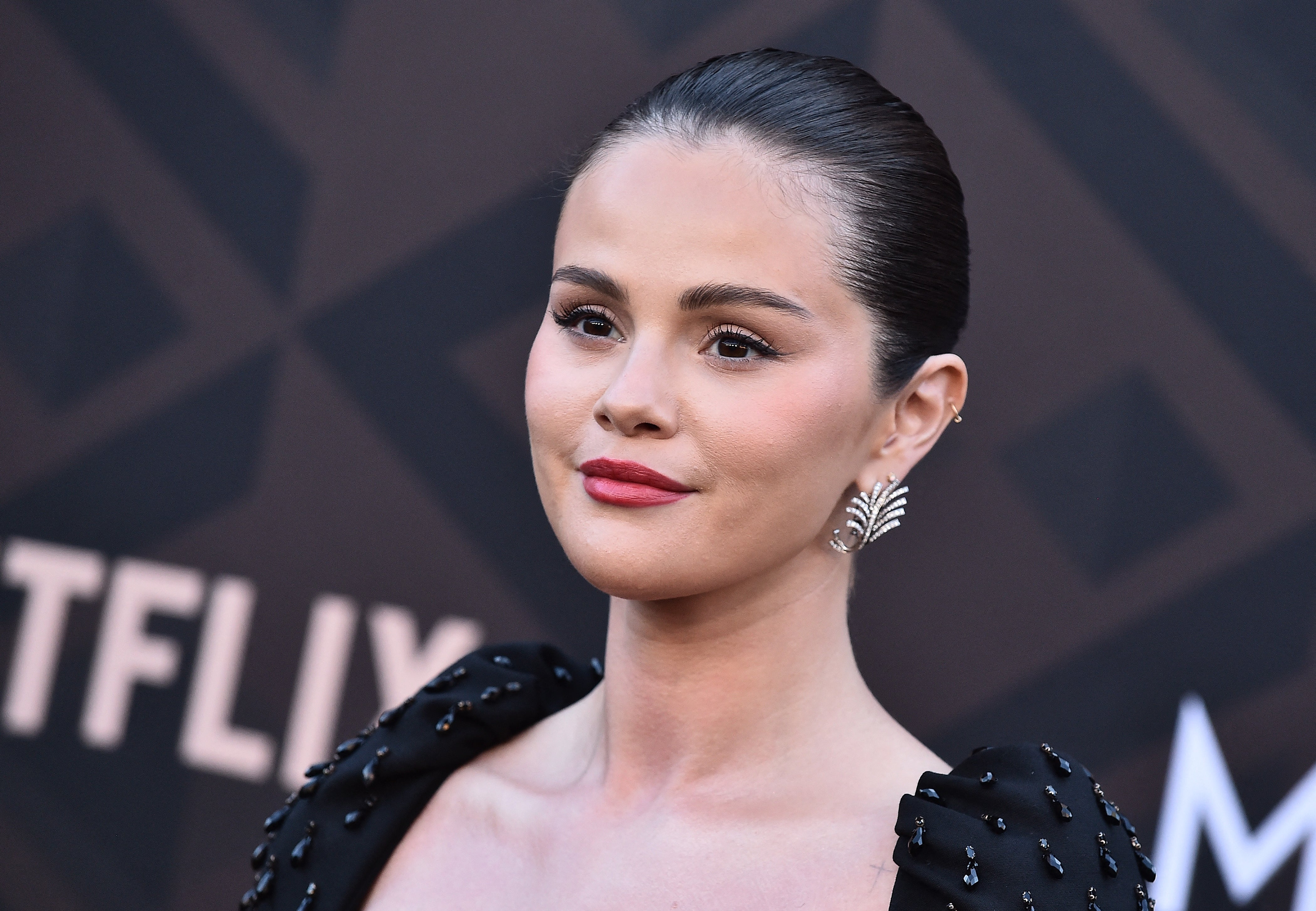 Person at an event in elegant attire with jeweled shoulder details, styled hair, and leaf-shaped earrings