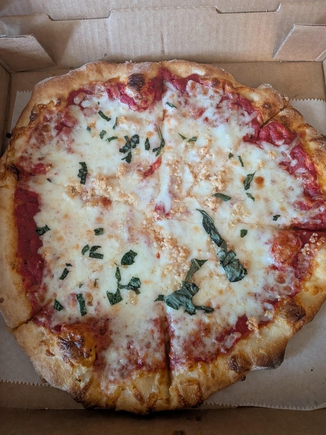 Pizza successful  a cardboard box, topped with cheese, herb  sauce, and basil leaves, sliced into portions