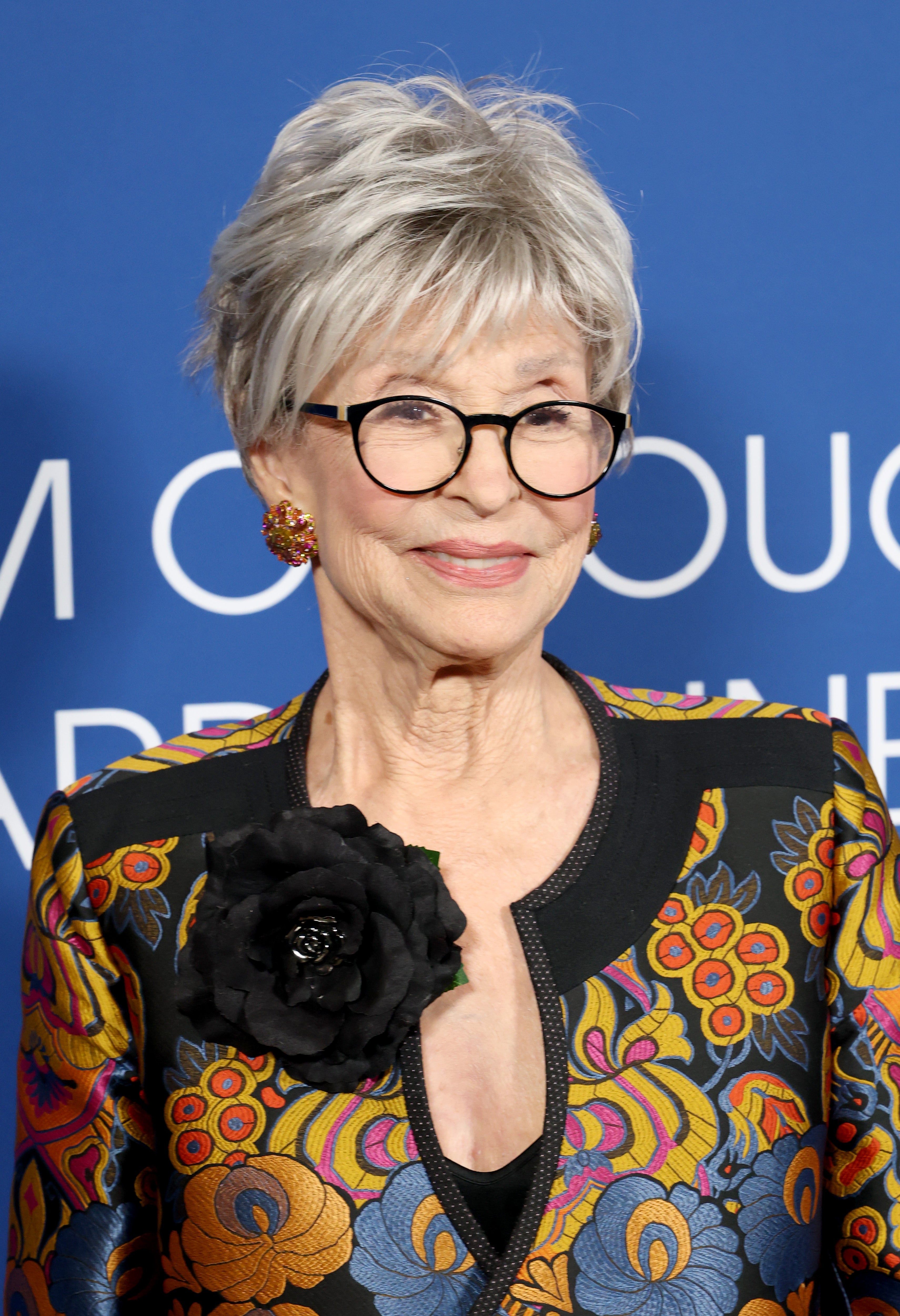 Person wearing glasses, floral-patterned jacket with large flower detail, at a formal event