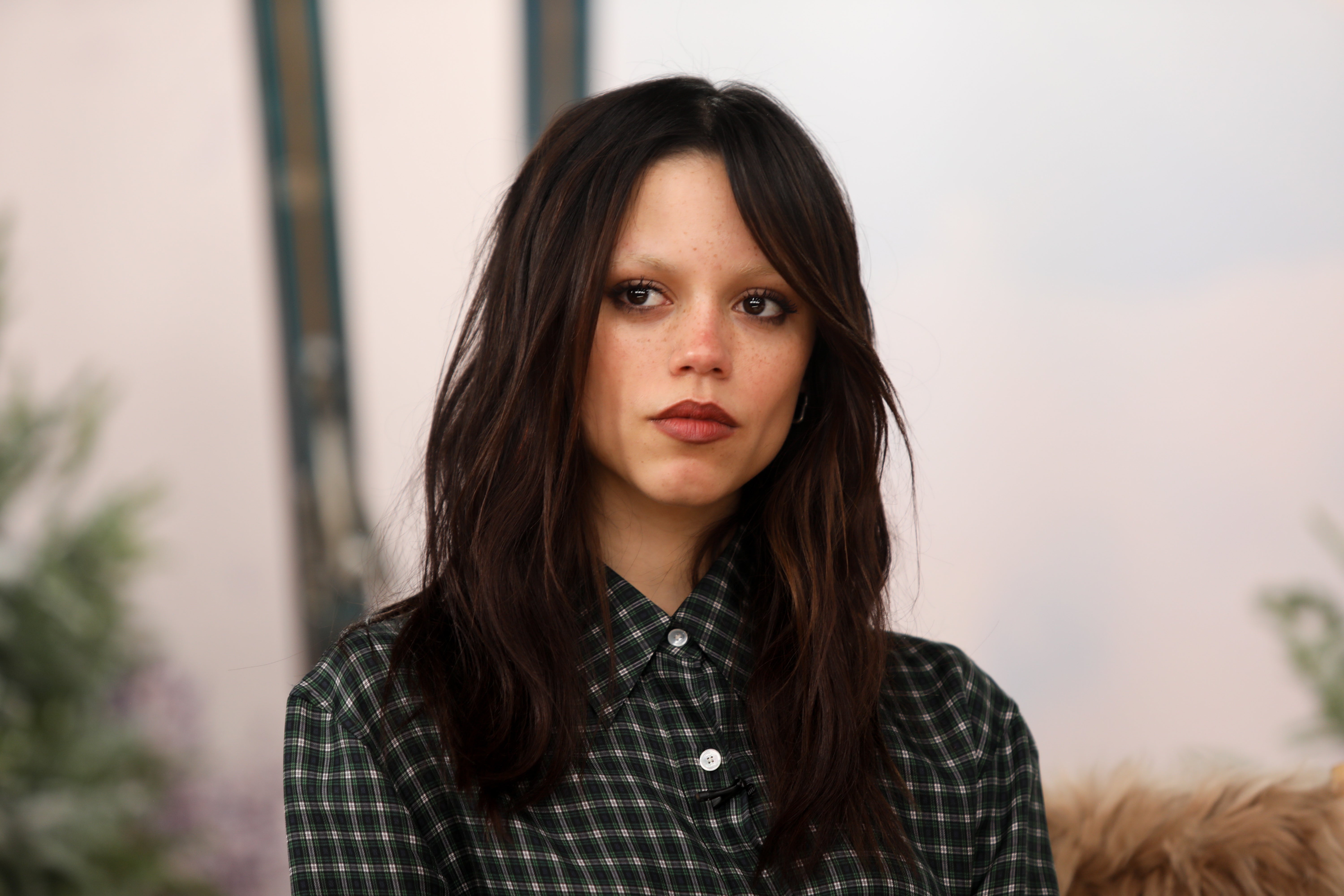 Person with long dark hair wearing a checked blouse, sitting in a casual setting