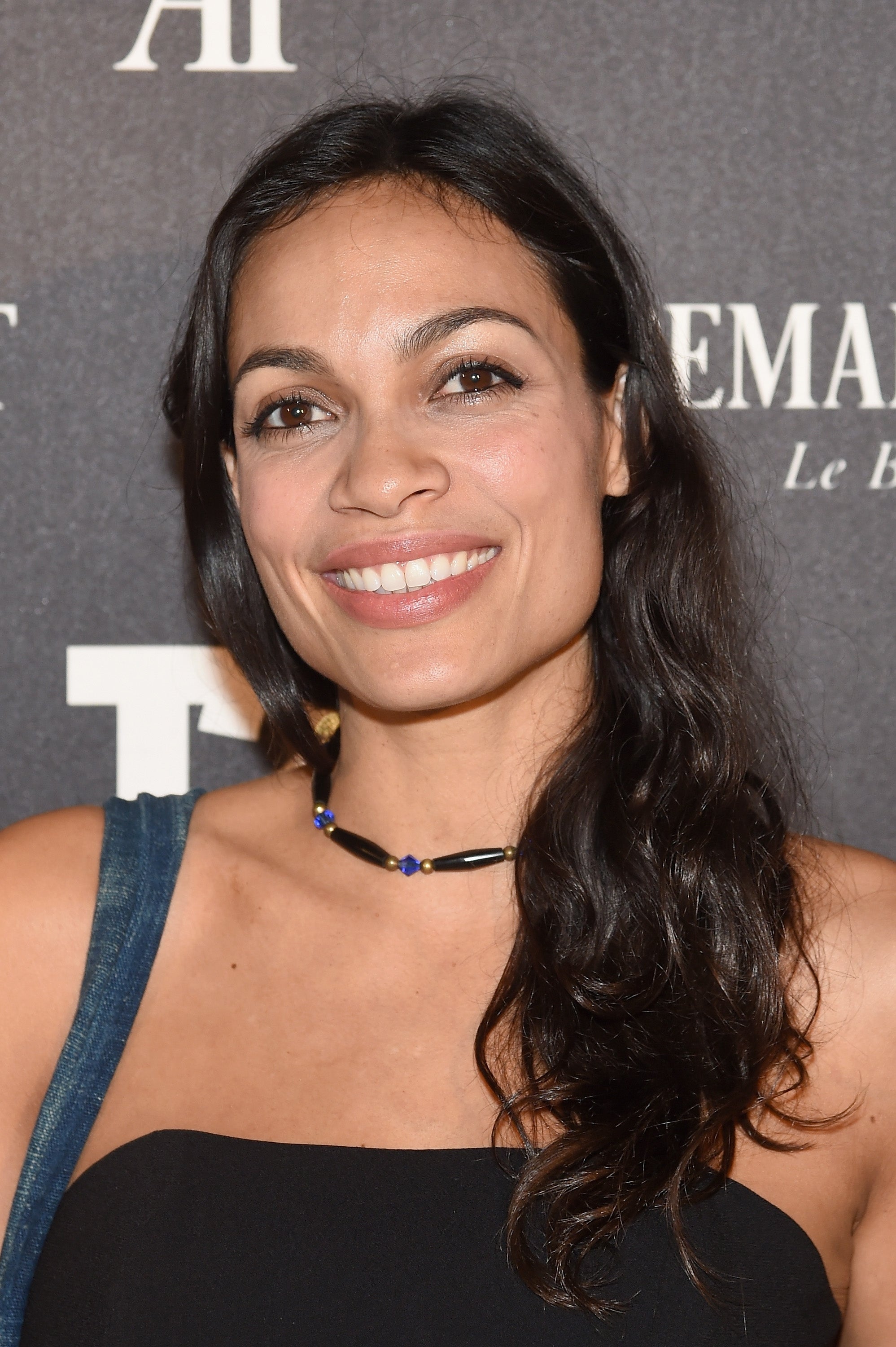 A person smiling at an event, wearing a strapless outfit with a bead necklace