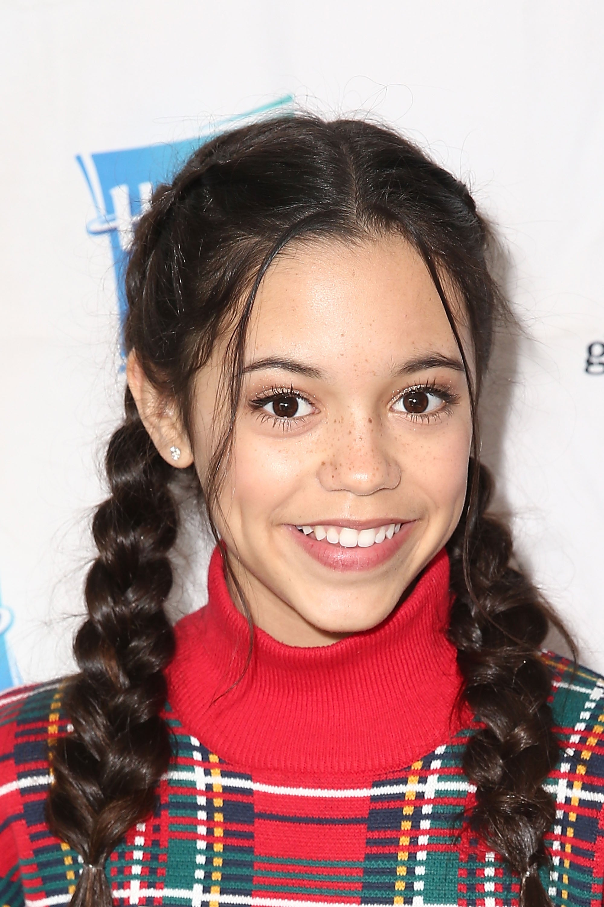 Person with braided hair smiling, wearing a plaid outfit with a red turtleneck