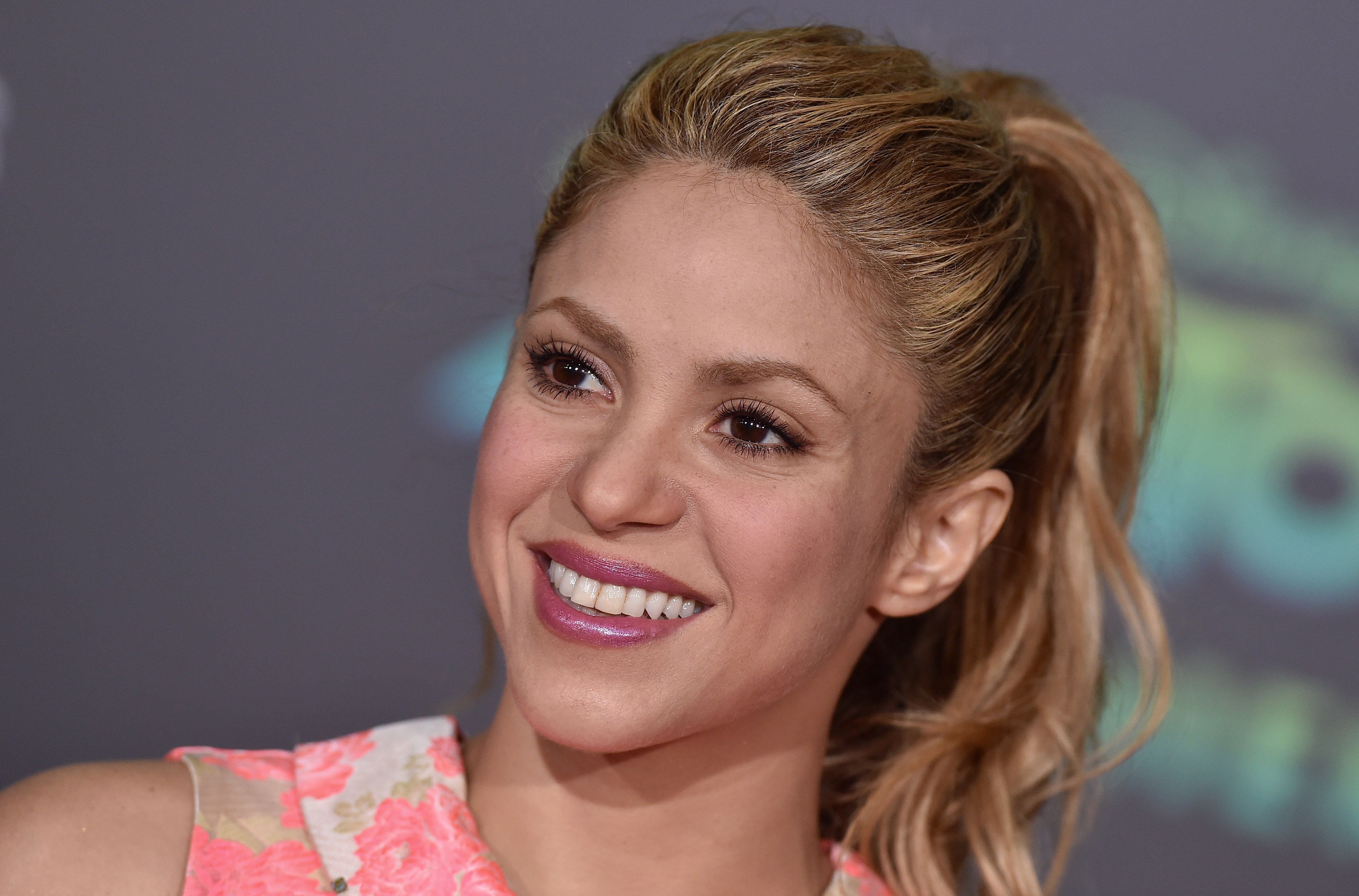 Woman smiling with a floral dress, wearing her hair in a high ponytail, appearing at a public event