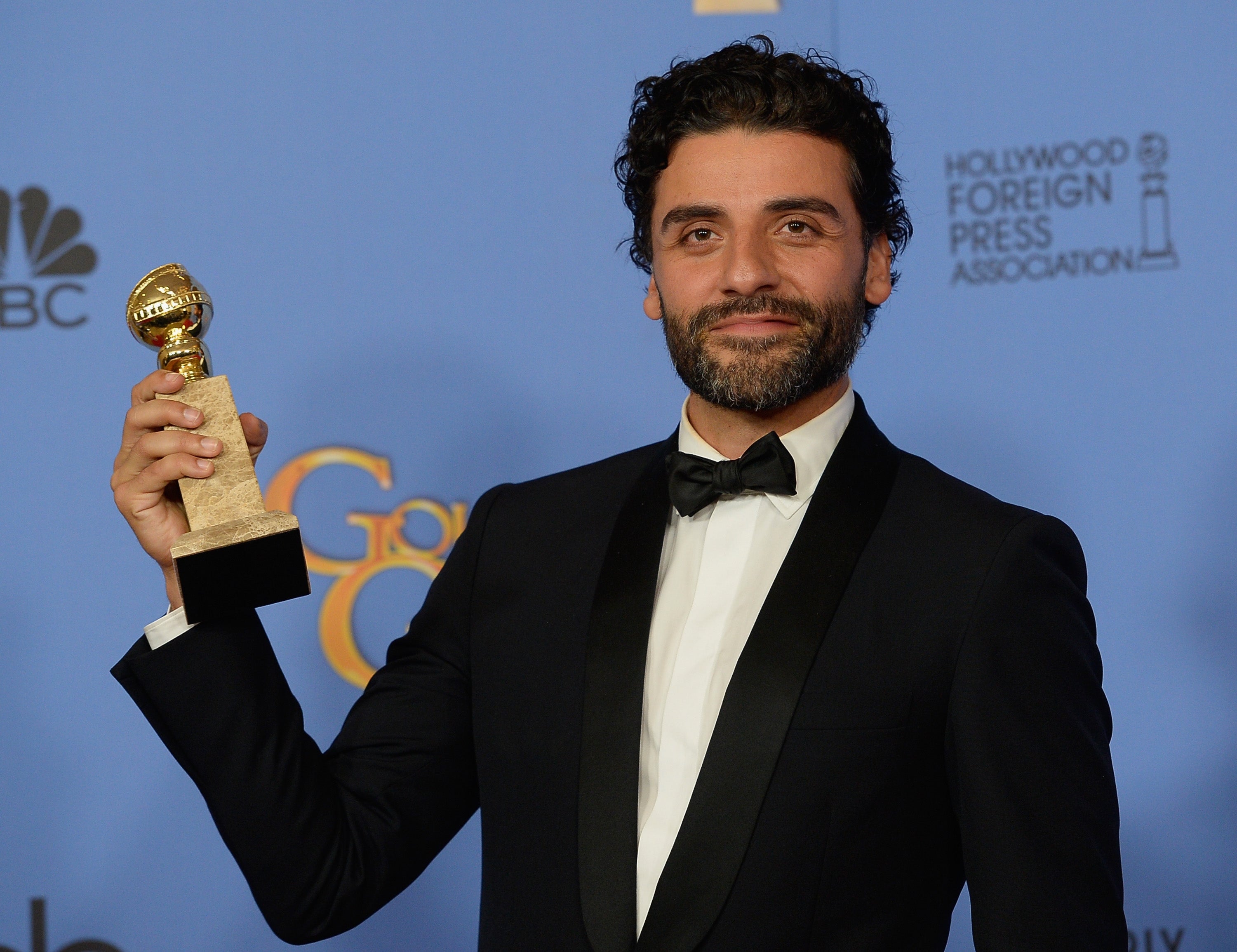 Person holding an award, wearing a formal suit and bow tie, in front of a backdrop with logos