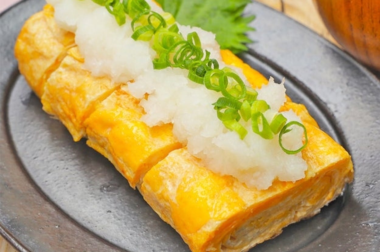 大根おろしとねぎを添えた卵焼きが黒い皿に盛られている。