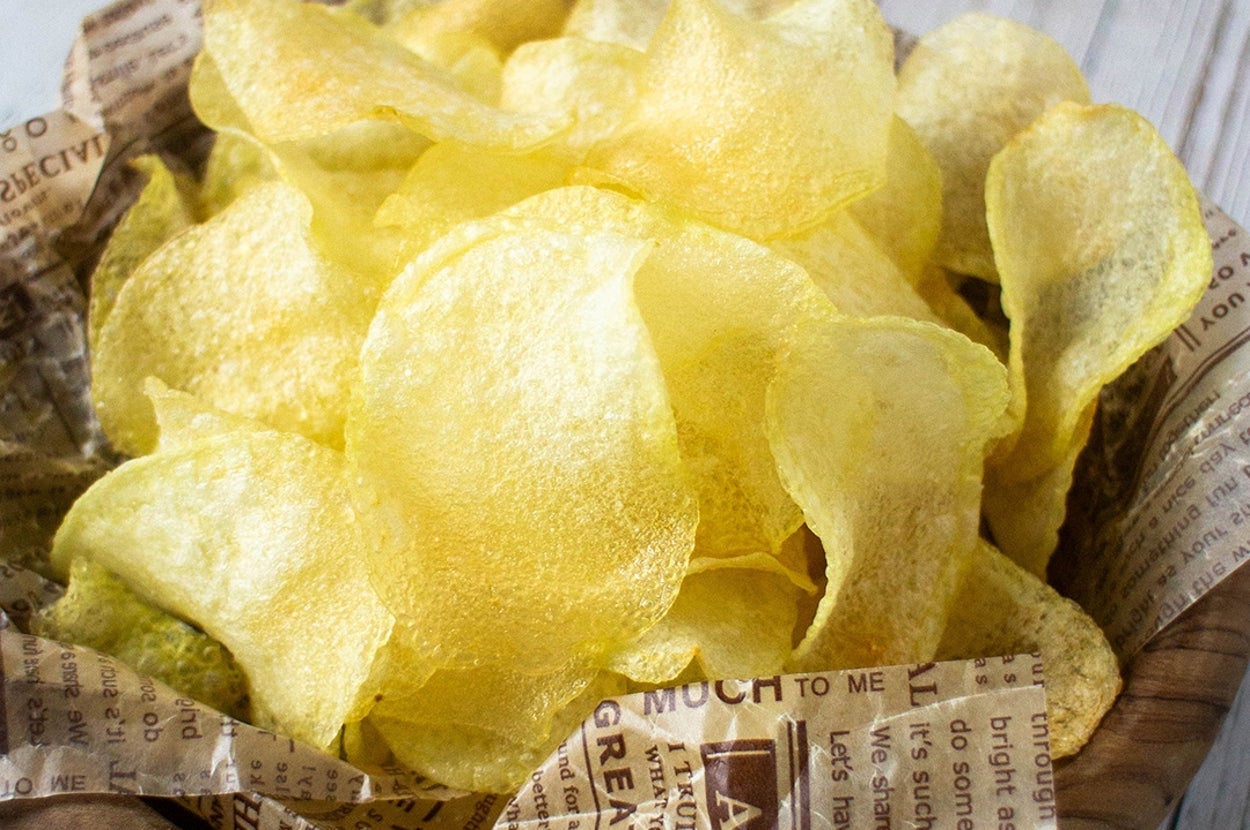 ボウルに盛られた薄くカットされたポテトチップス。新聞の様な紙に載せられている。