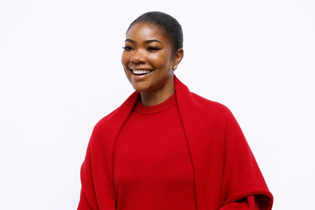 Smiling person wearing a sleek red dress and matching shawl, styled hair pulled back