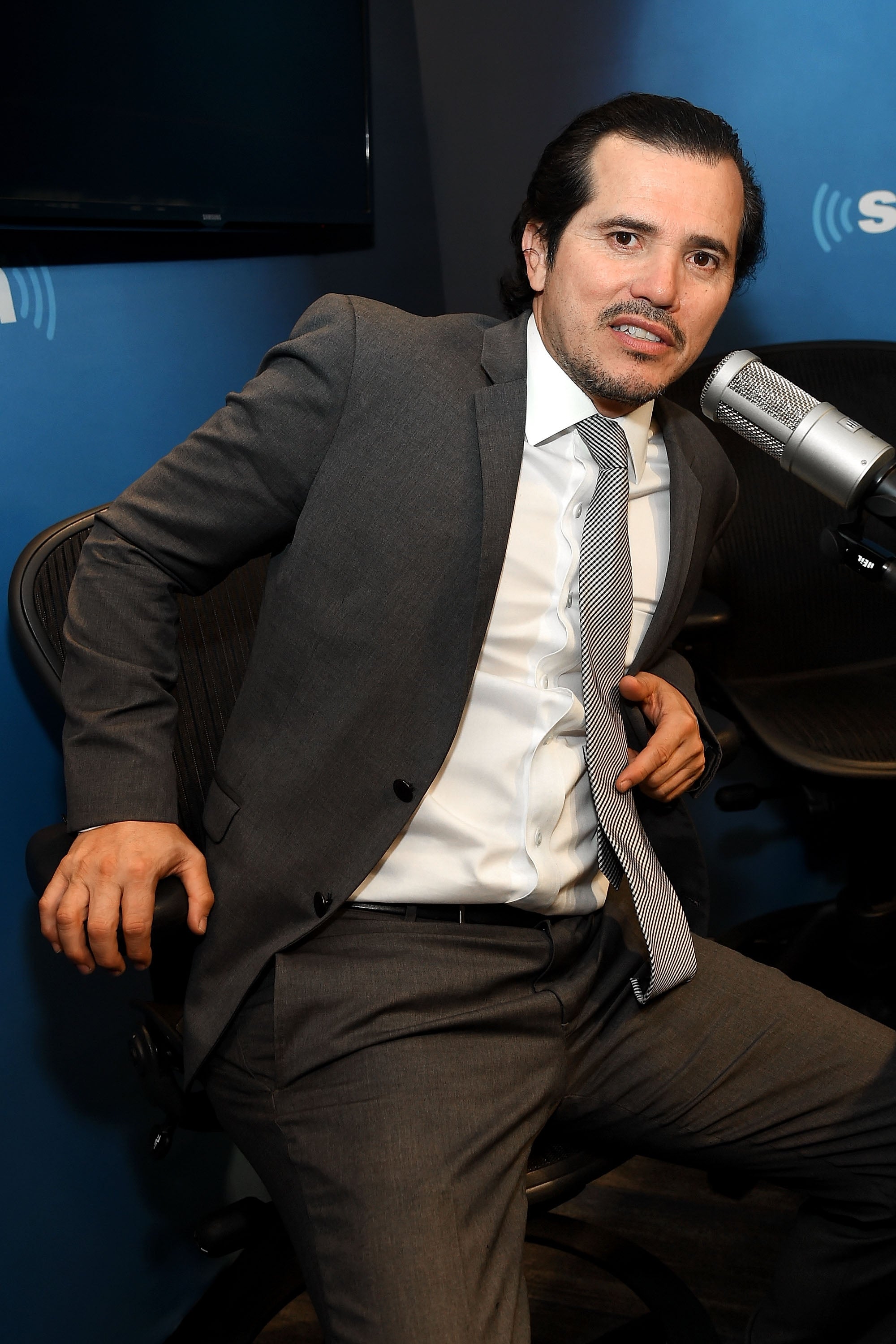 Person in a suit and tie sits in a radio studio, speaking into a microphone