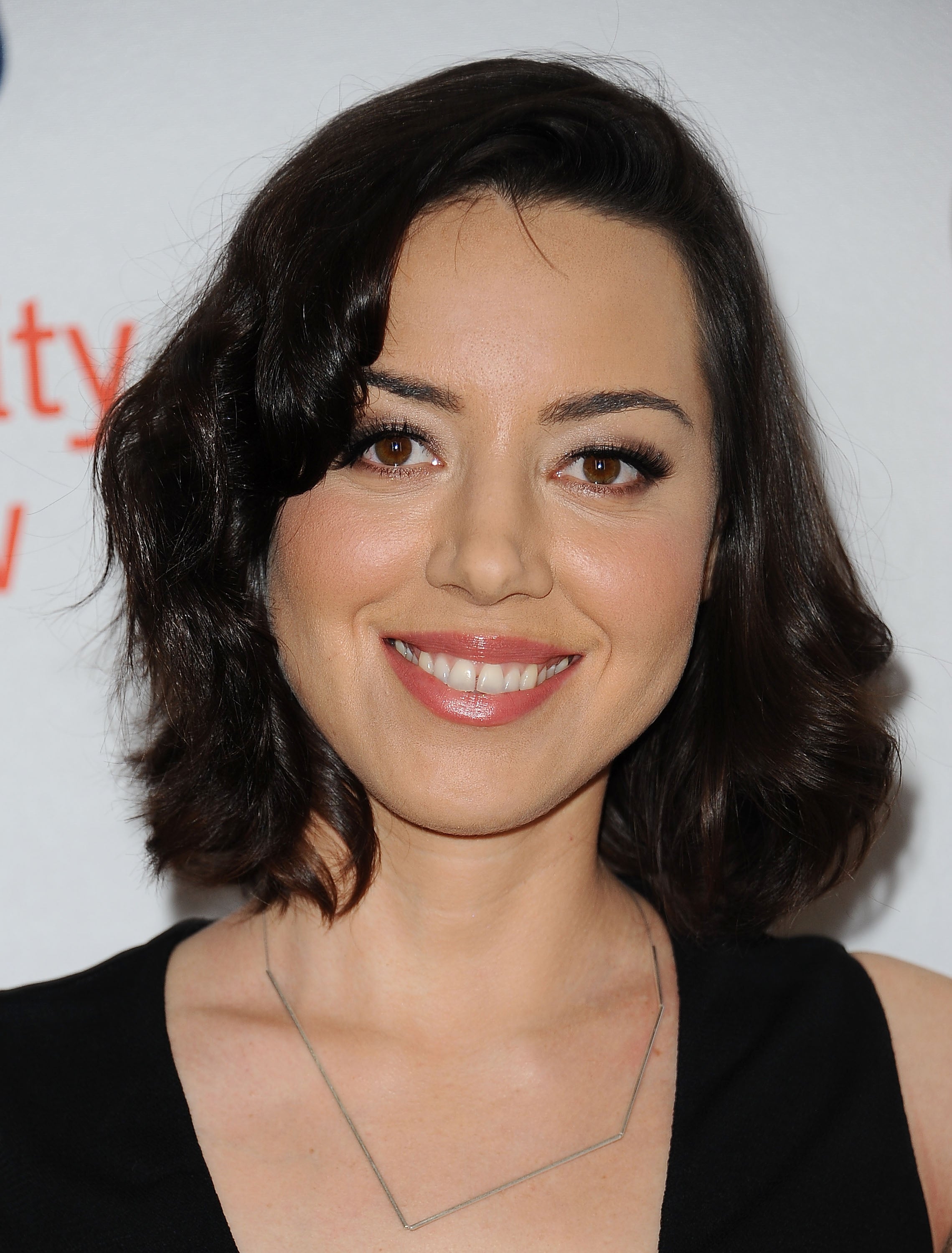 Person smiling at an event, wearing a sleeveless black top and a delicate geometric necklace