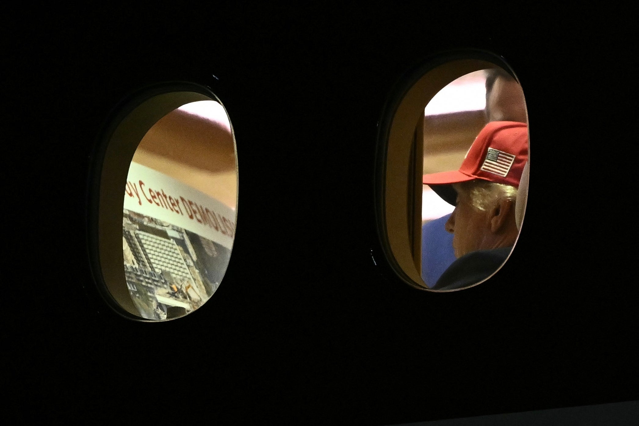 En person i en rød lue med et amerikansk flagg sees gjennom et flyvindu, og ser ut på en flyplassterminal