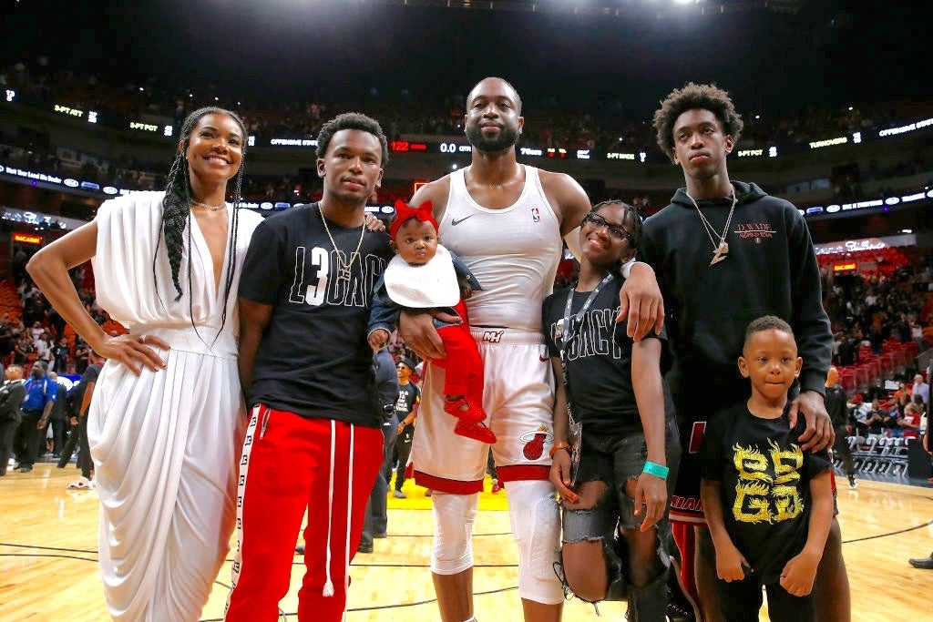 A group stands on a basketball court; one person wears a sports uniform, others in casual attire, celebrating an event