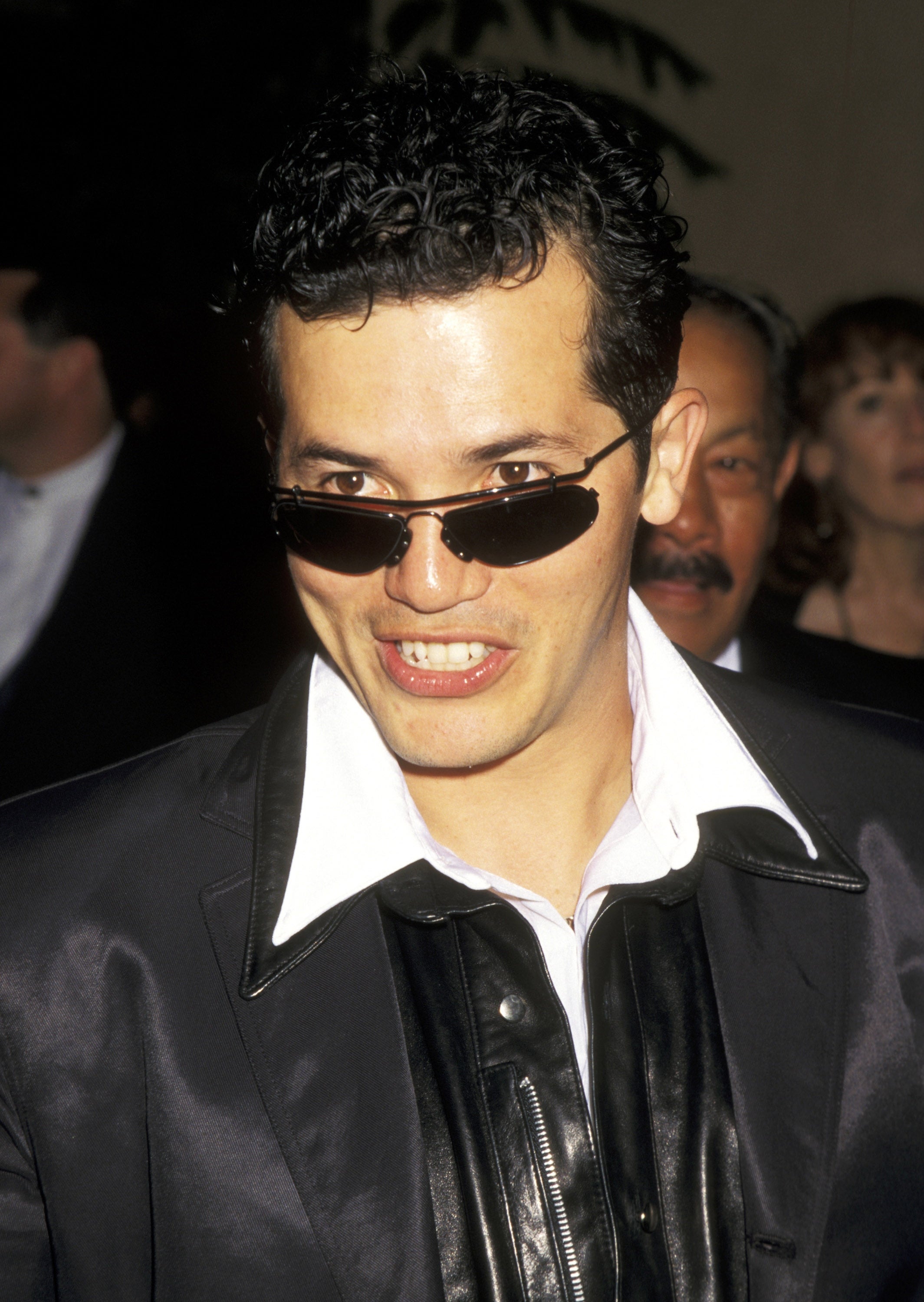 Person in a stylish suit and sunglasses at an event, speaking energetically