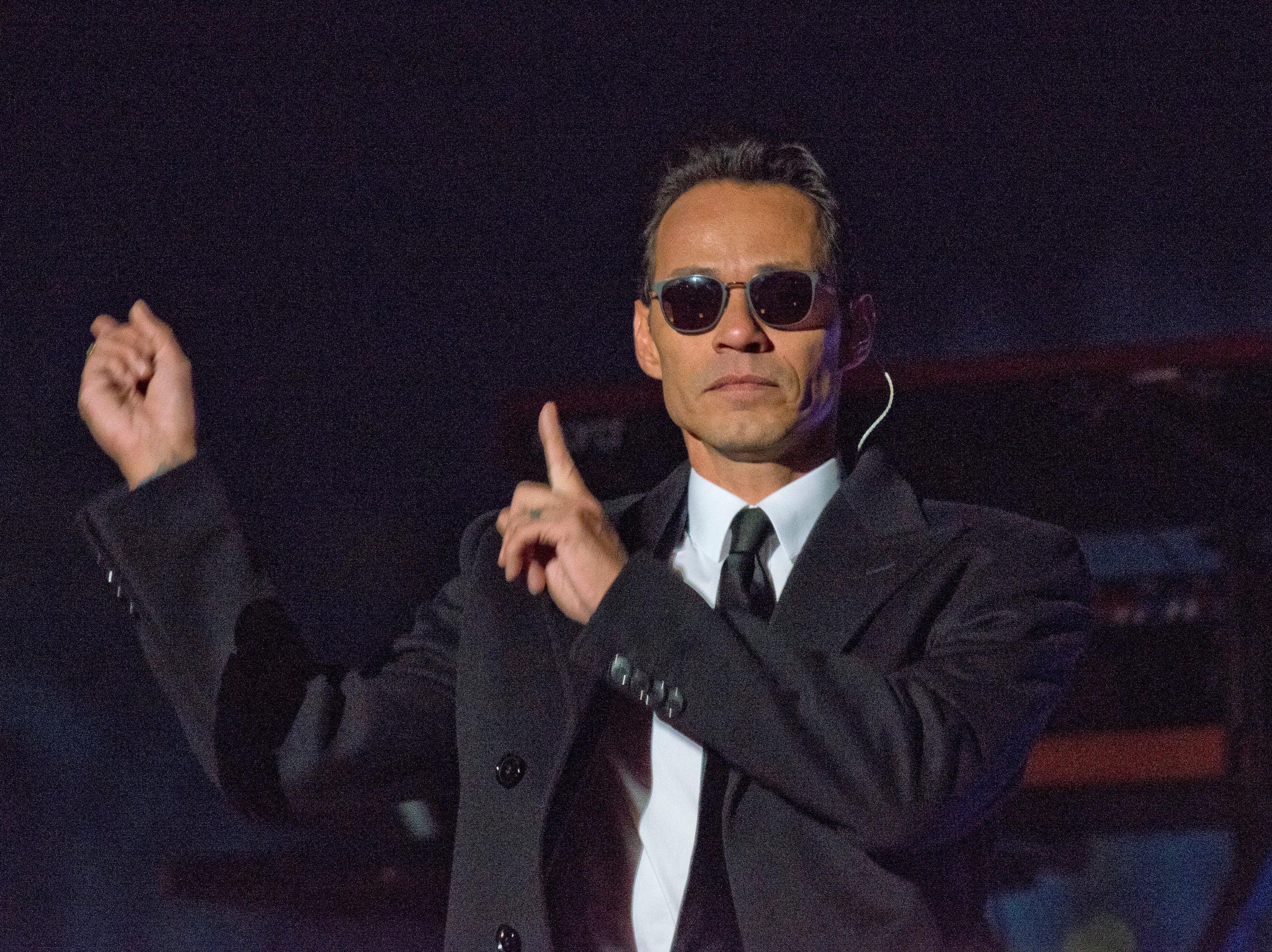 Person in a suit and sunglasses, performing on stage, pointing with both hands