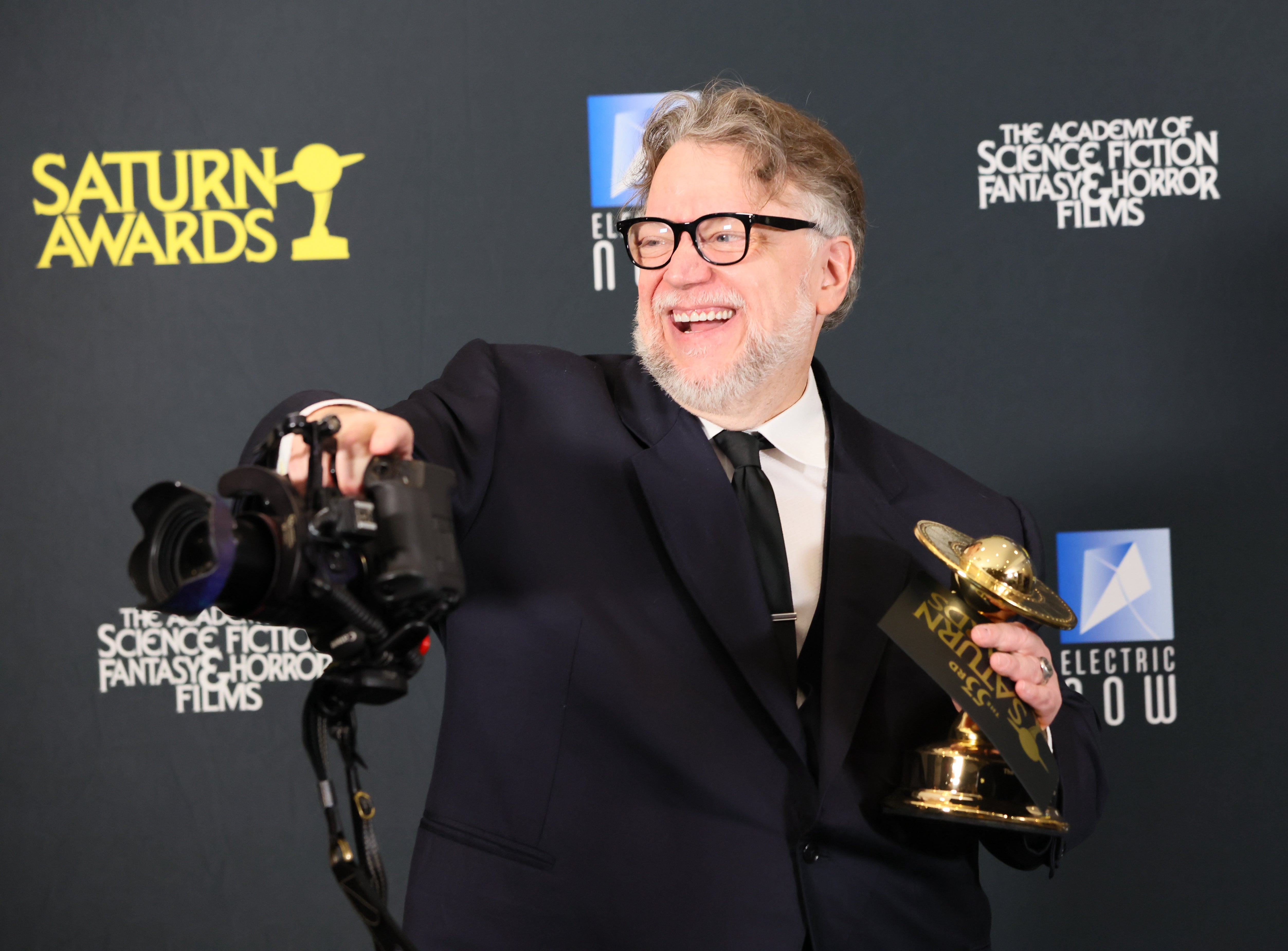 Man in suit holding a Saturn Award, smiling and posing for photos at an award event