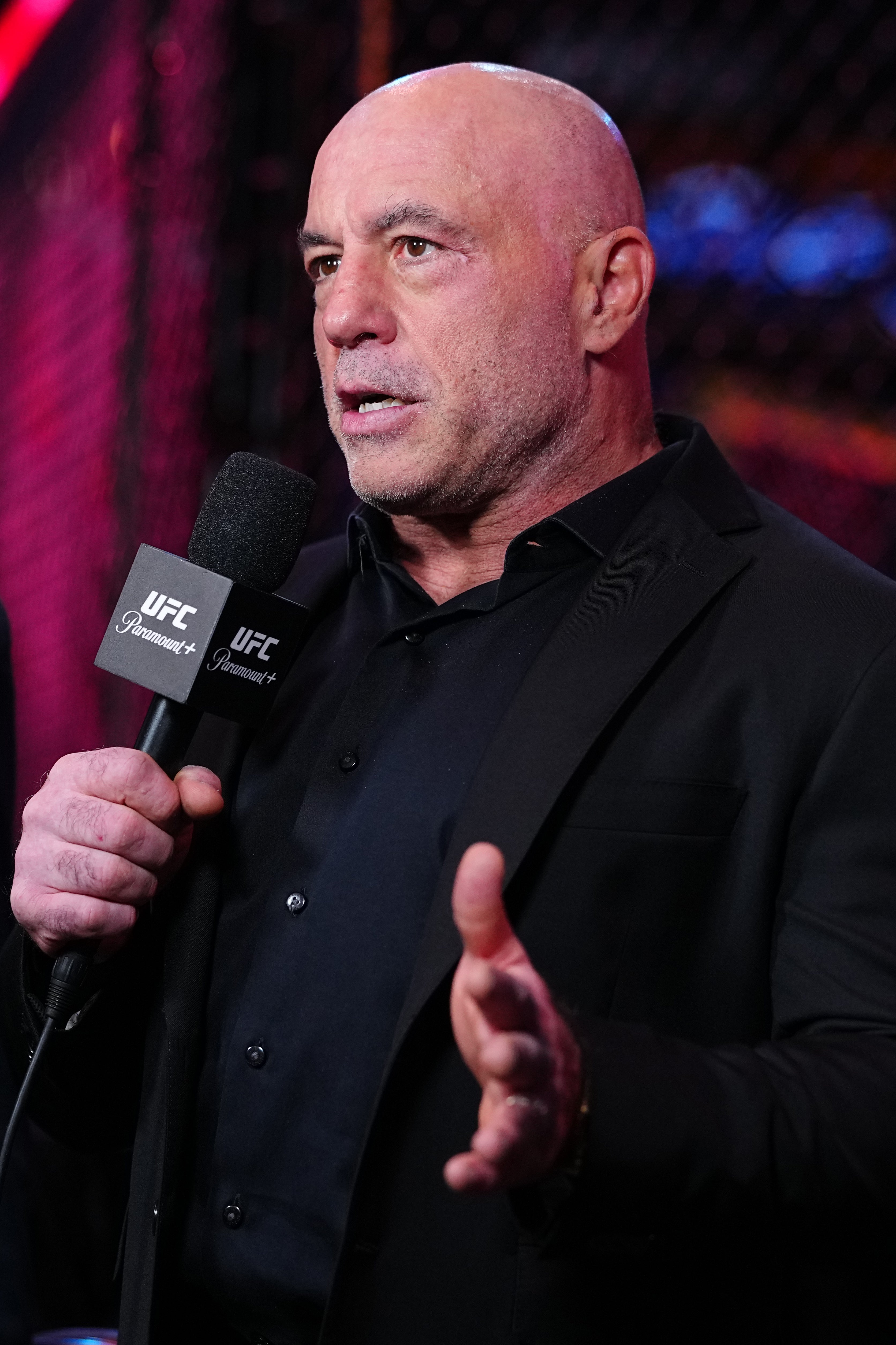 En person som har på seg en svart dress holder en mikrofon med en UFC-etikett, og ser ut til å snakke på et arrangement