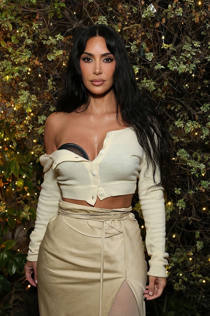 Person in an off-shoulder top and skirt poses outdoors in front of a leafy backdrop with decorative lights